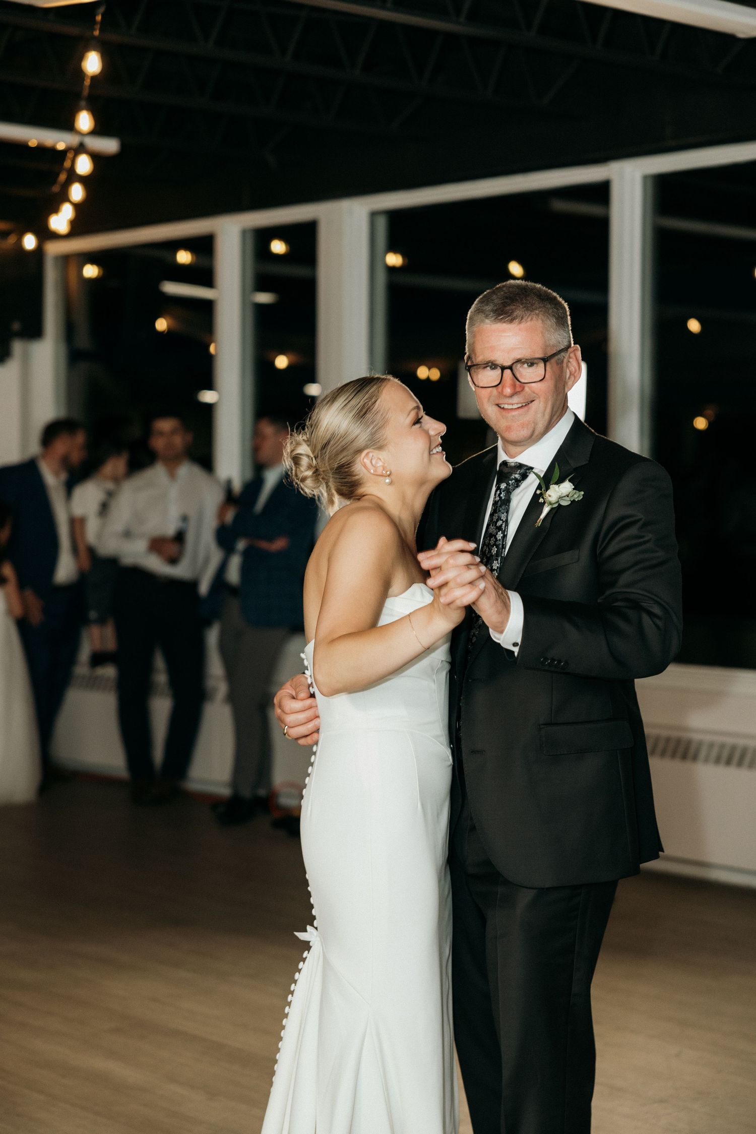 A couple shares an intimate dance together at their wedding reception under string lights.