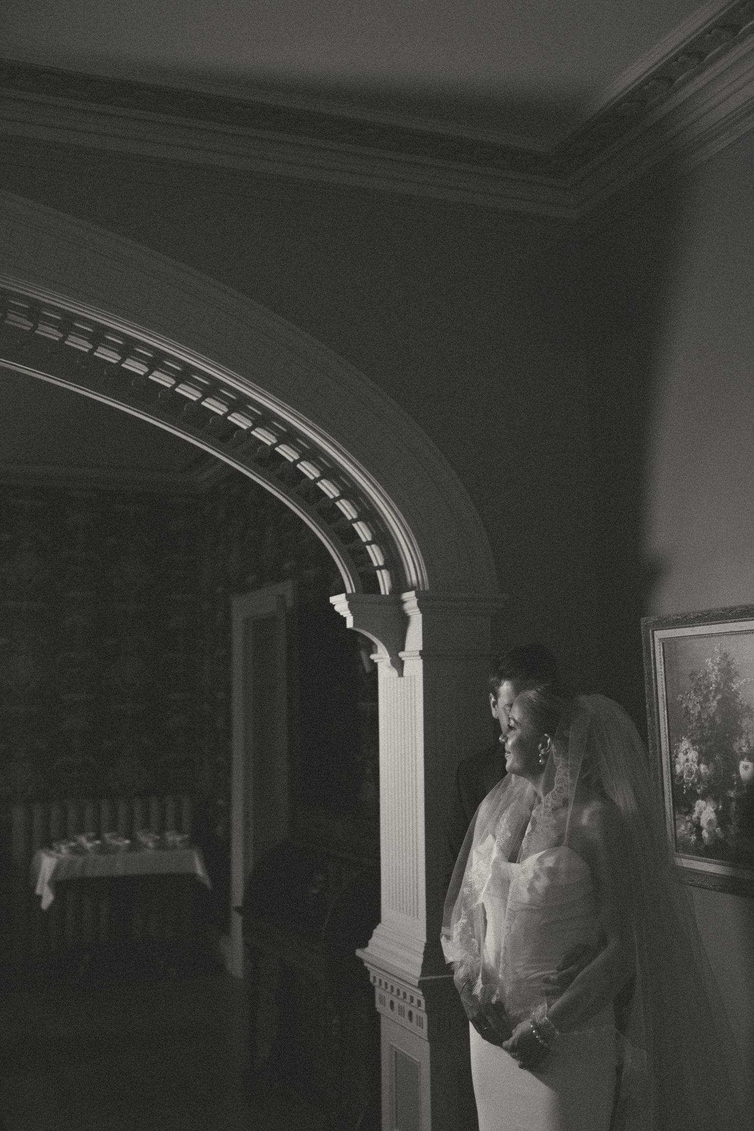 Black and white wedding photos captured under an arched doorway with dramatic lighting.