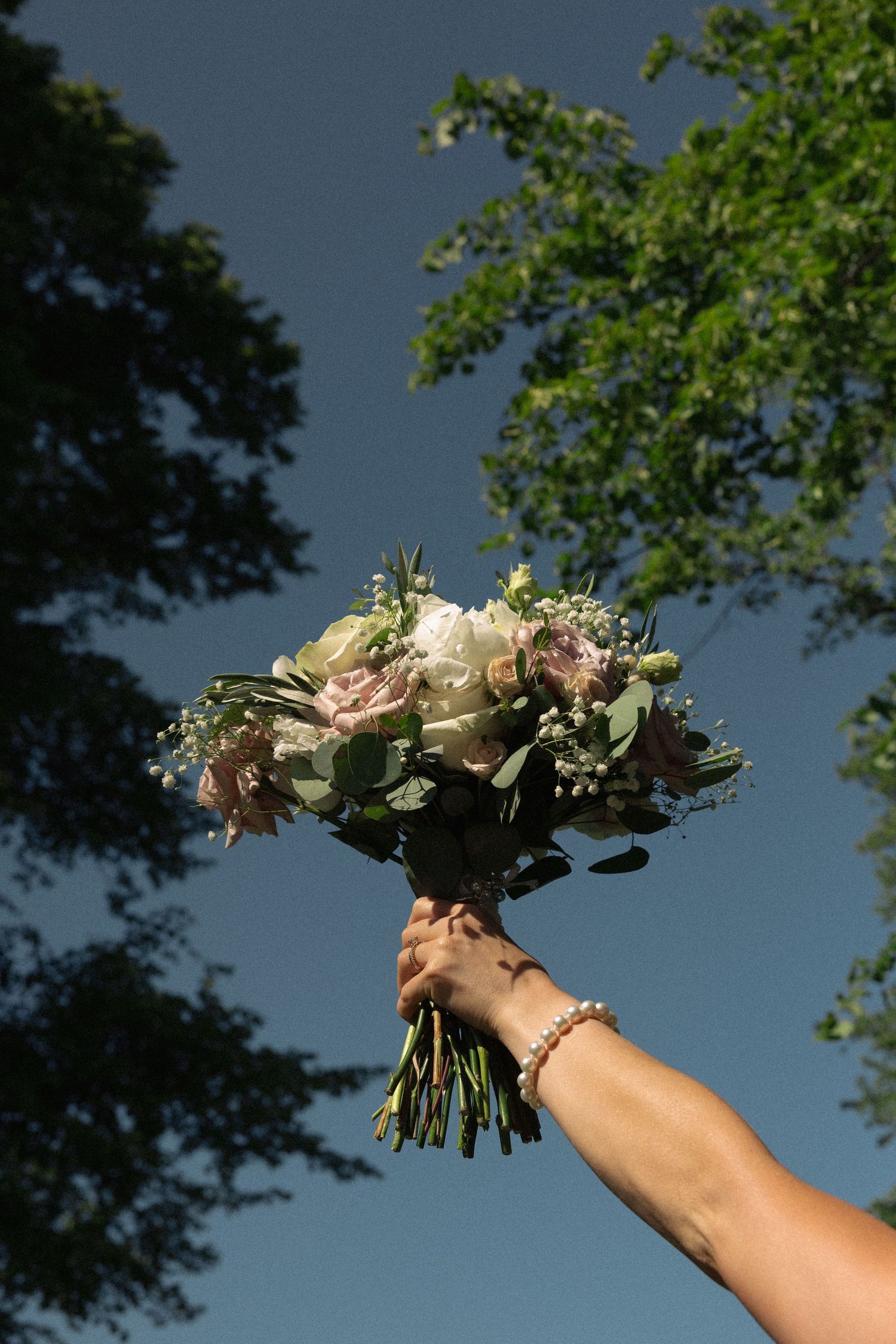 A bridal bouquet with blush roses and greenery held up against a dramatic sky.