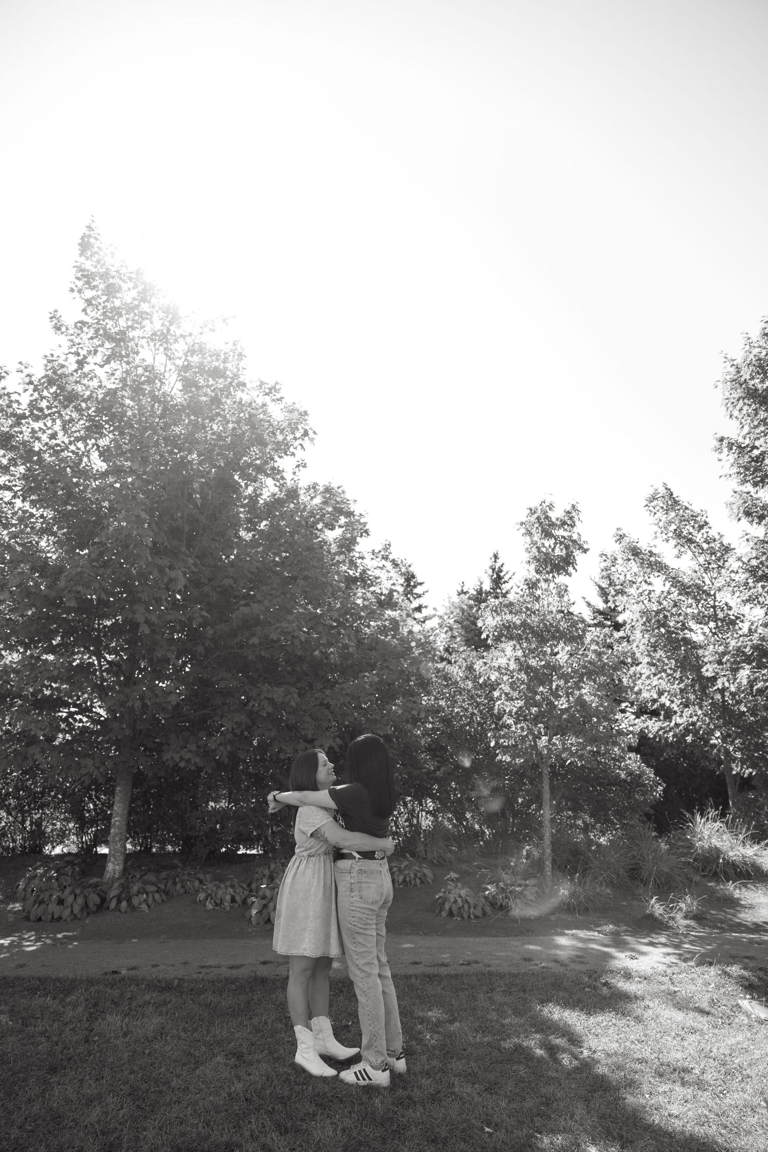Black and white photo of two people embracing in a park surrounded by trees.