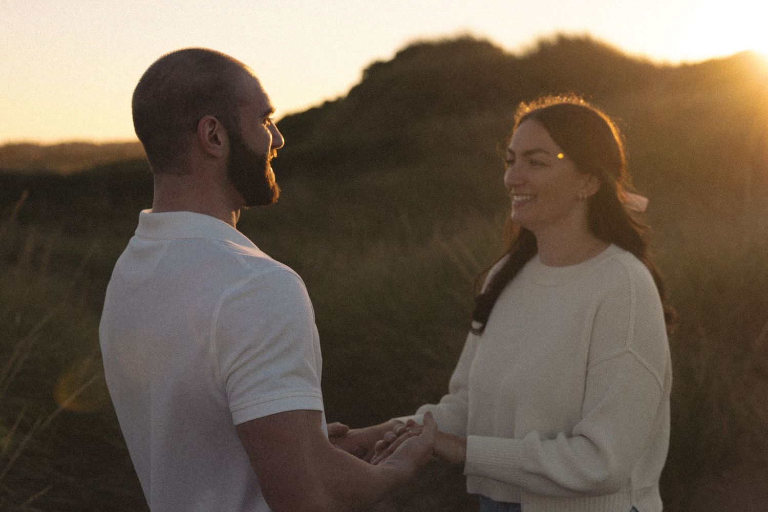 Couple in casual attire shares tender moment in golden sunset light on beach.