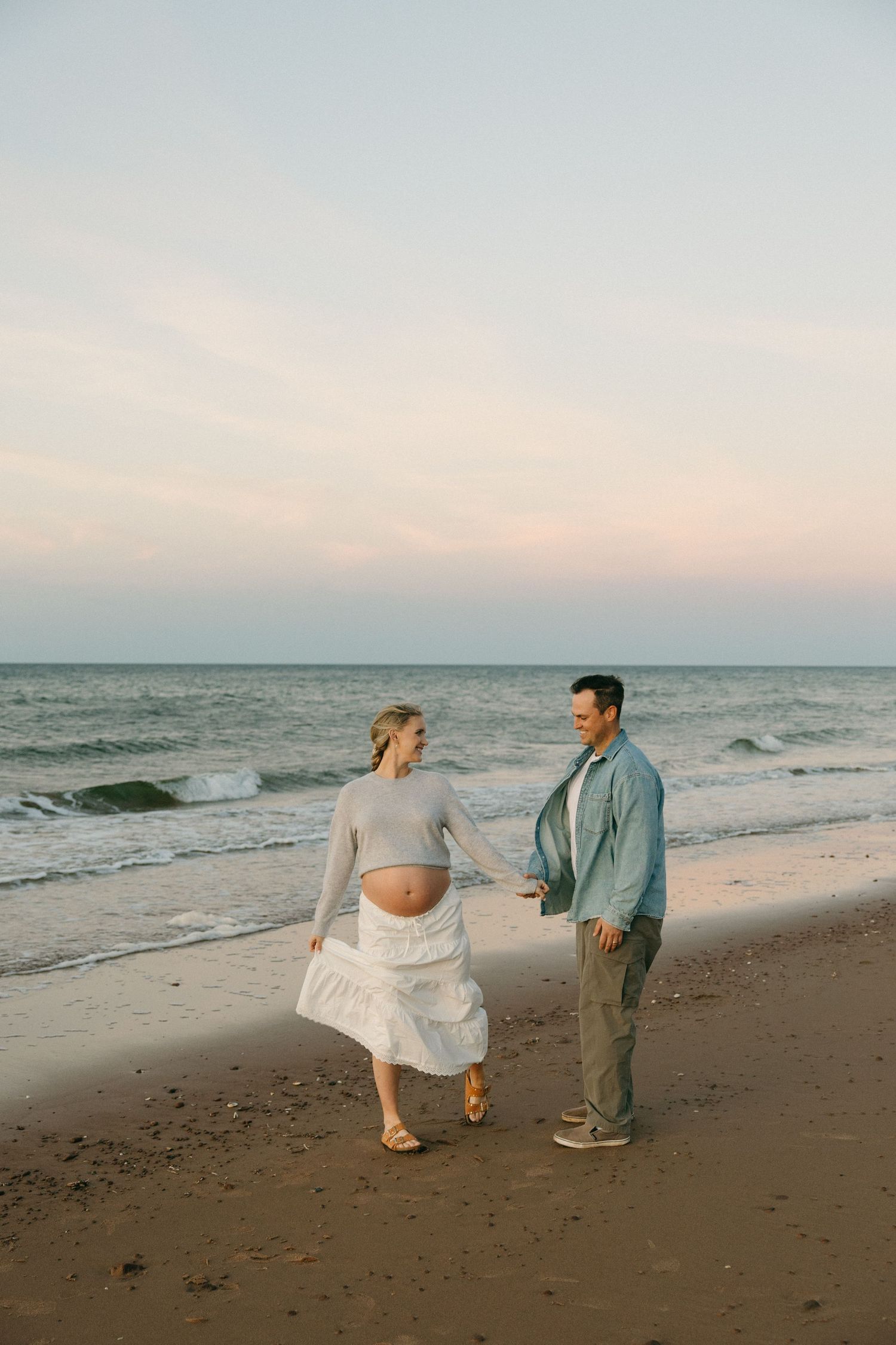 Two people dance and play together on a sandy beach at sunset.