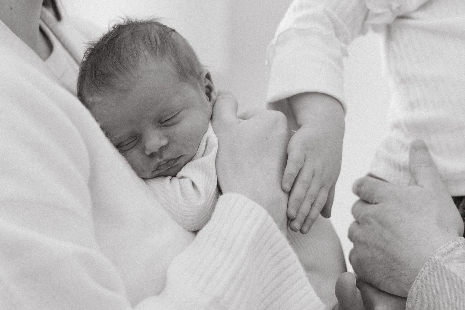 A newborn baby sleeps peacefully while being cradled in soft white blankets.