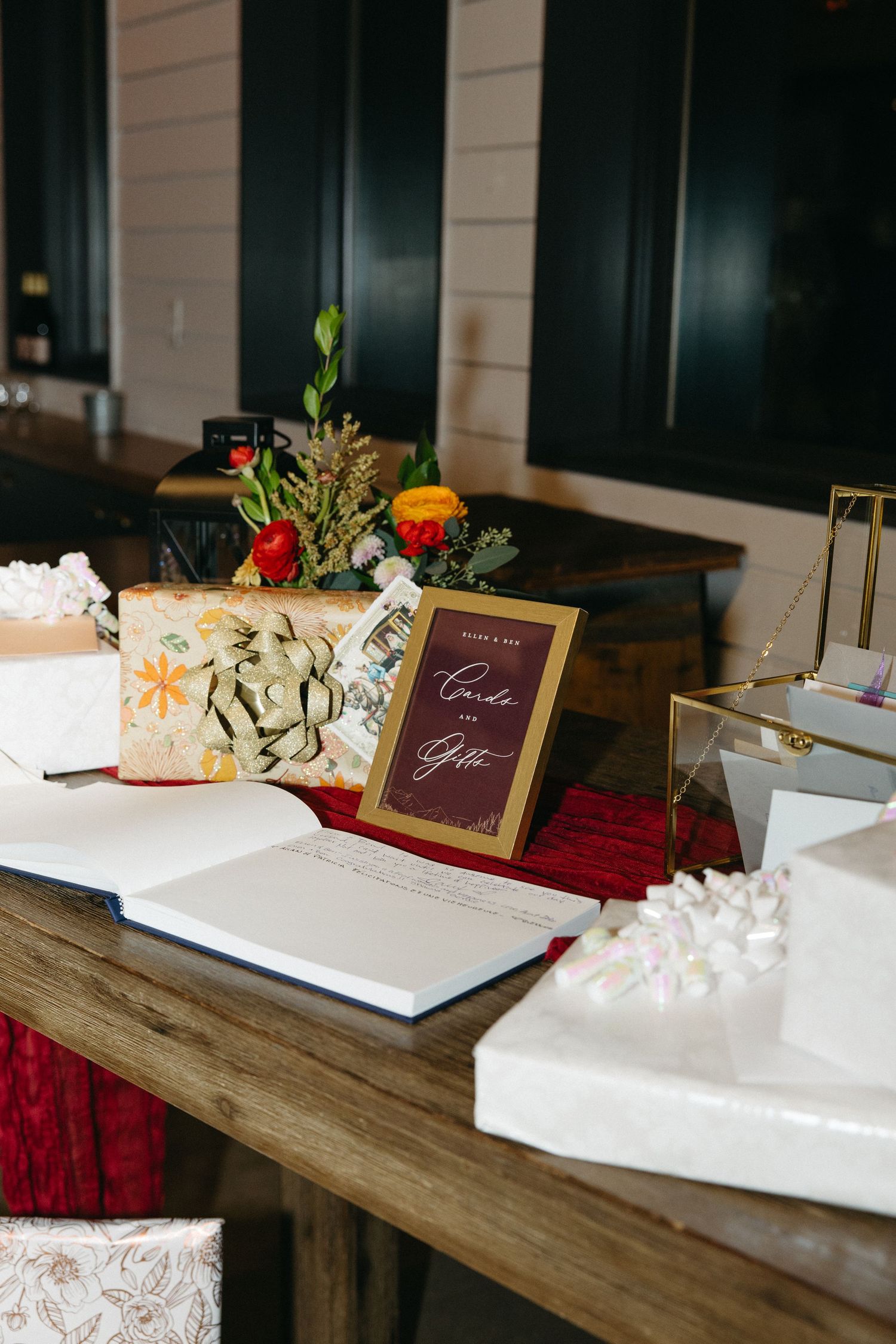 Rustic wooden guest book table with burgundy accents and white floral decorations.