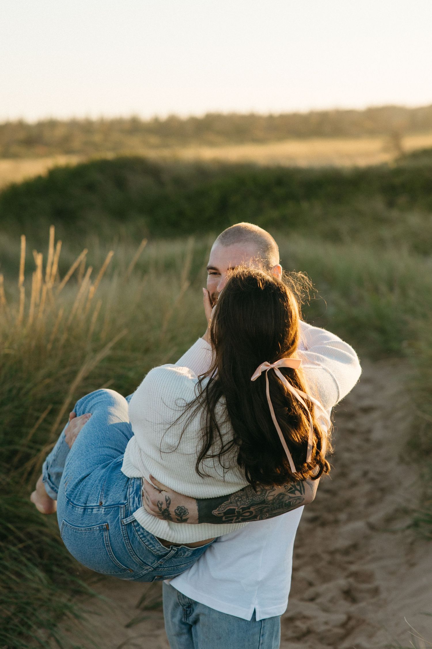 A playful couple dances and spins in a field of grass during sunset.
