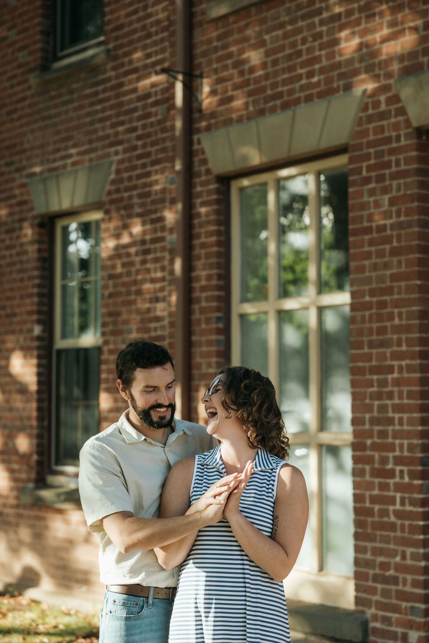 A couple shares a loving moment while holding hands against a brick facade.