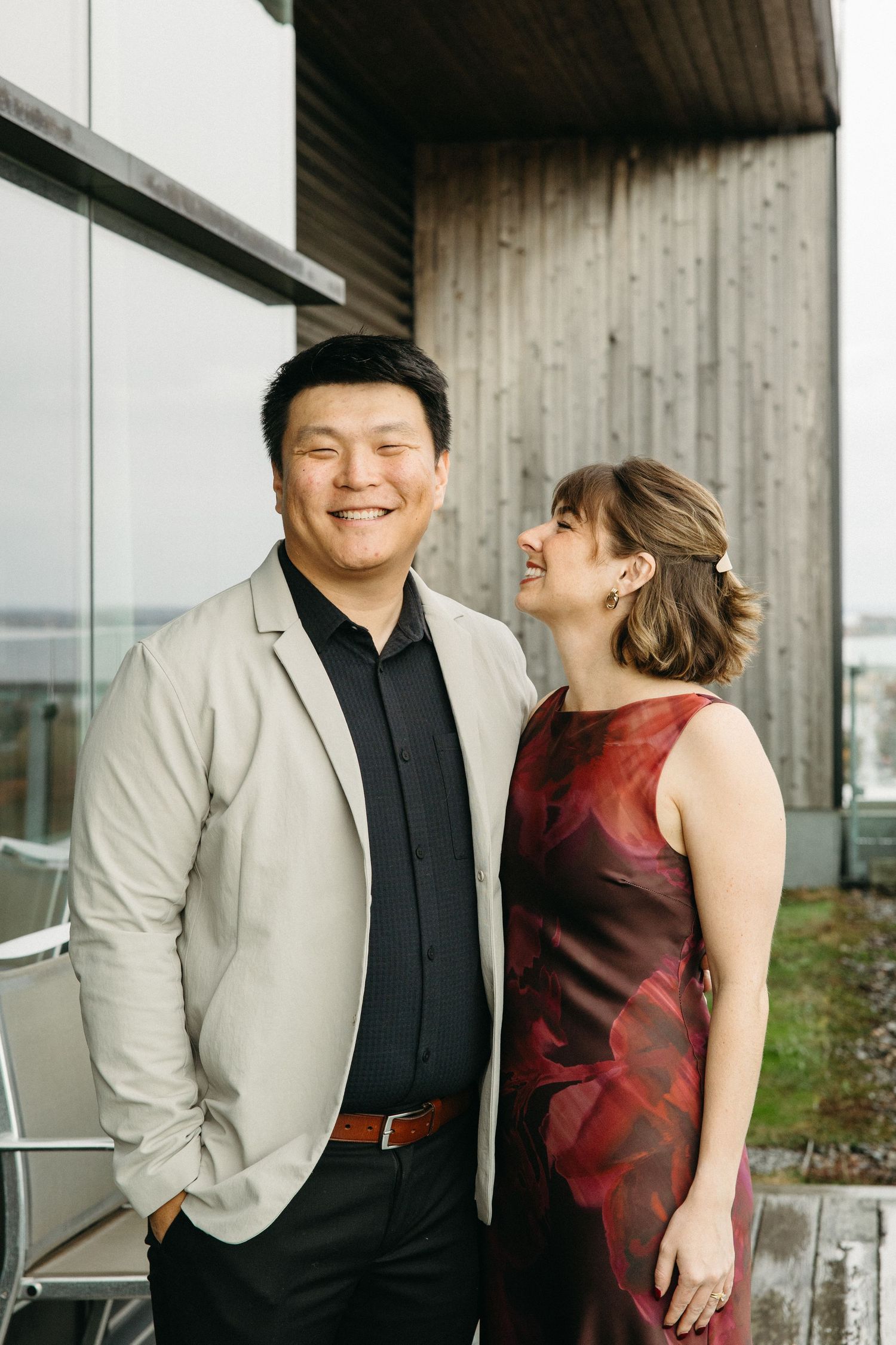 A couple in formal attire shares a tender moment against a modern architectural backdrop.