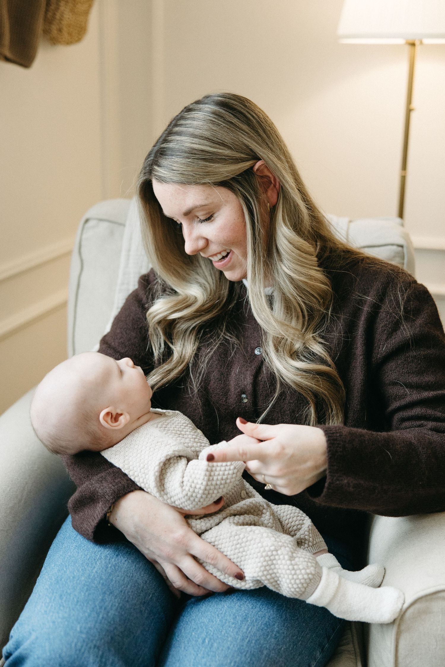 Tender moment with newborn wrapped in cream knit blanket on cozy chair.