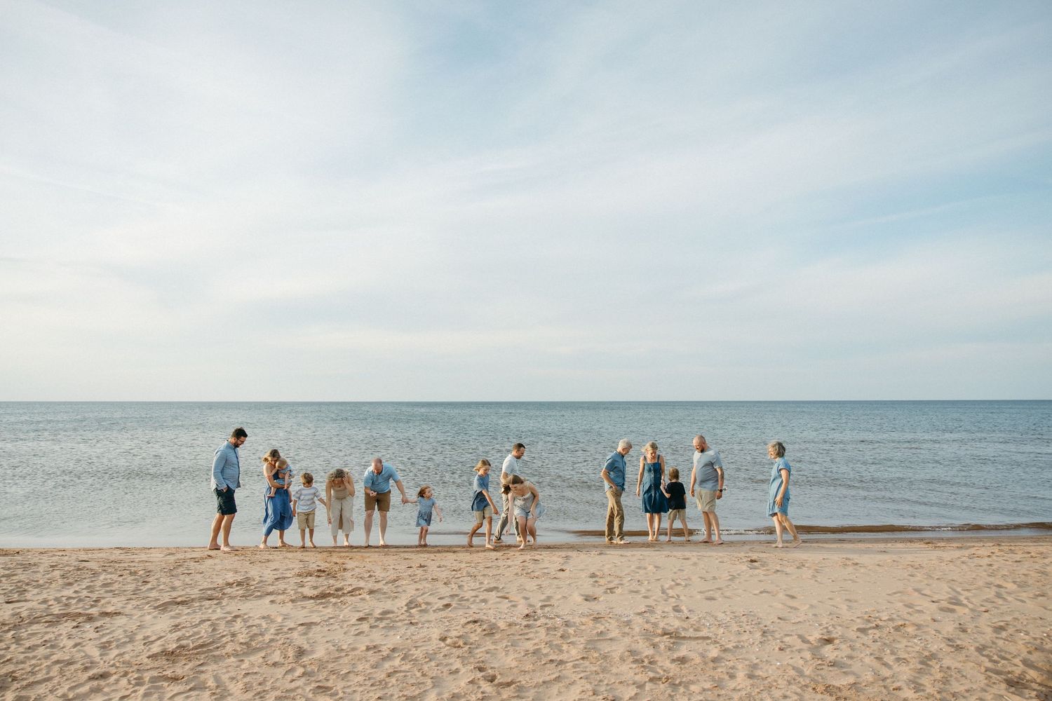 Extended family stands together along the shoreline gazing at the calm ocean during a beach photo session.