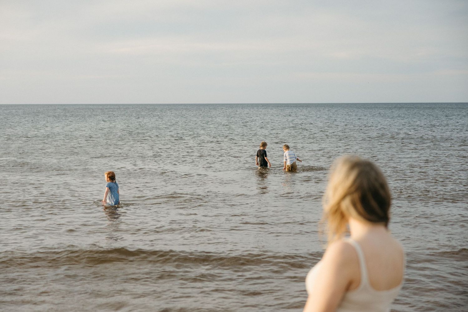 Group of people wading in calm ocean water on an overcast day at the beach.