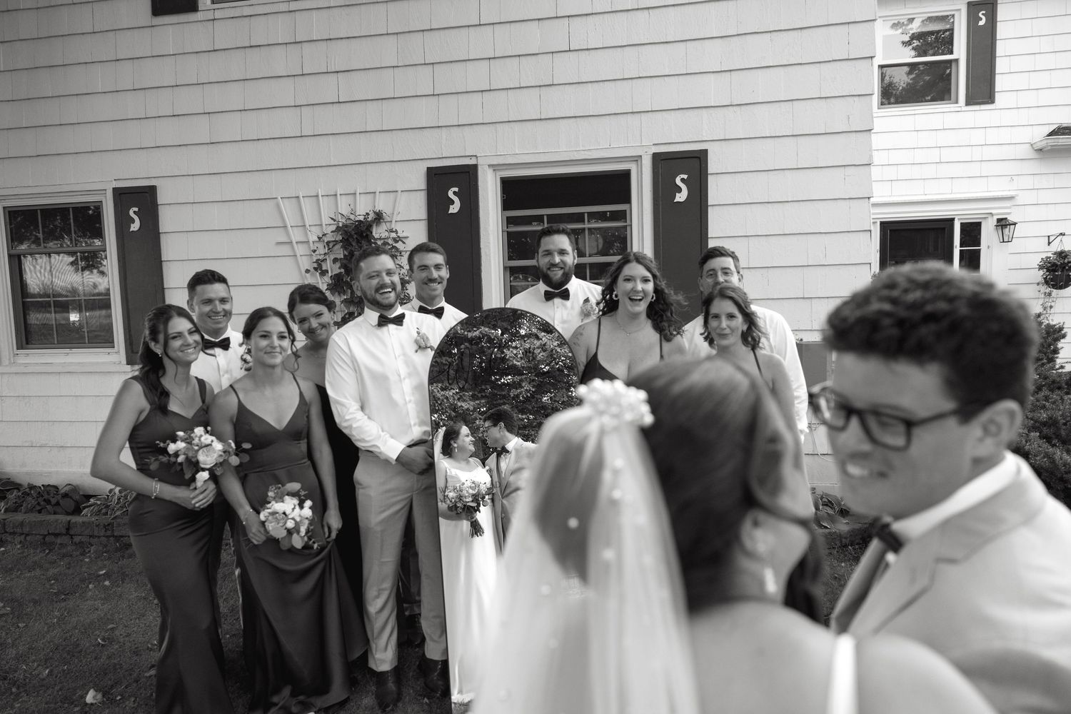 Wedding party posing together outside a white building in a black and white photo.