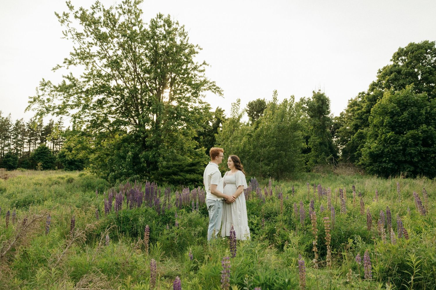 A romantic photoshoot in a meadow with tall grass and trees in the background.
