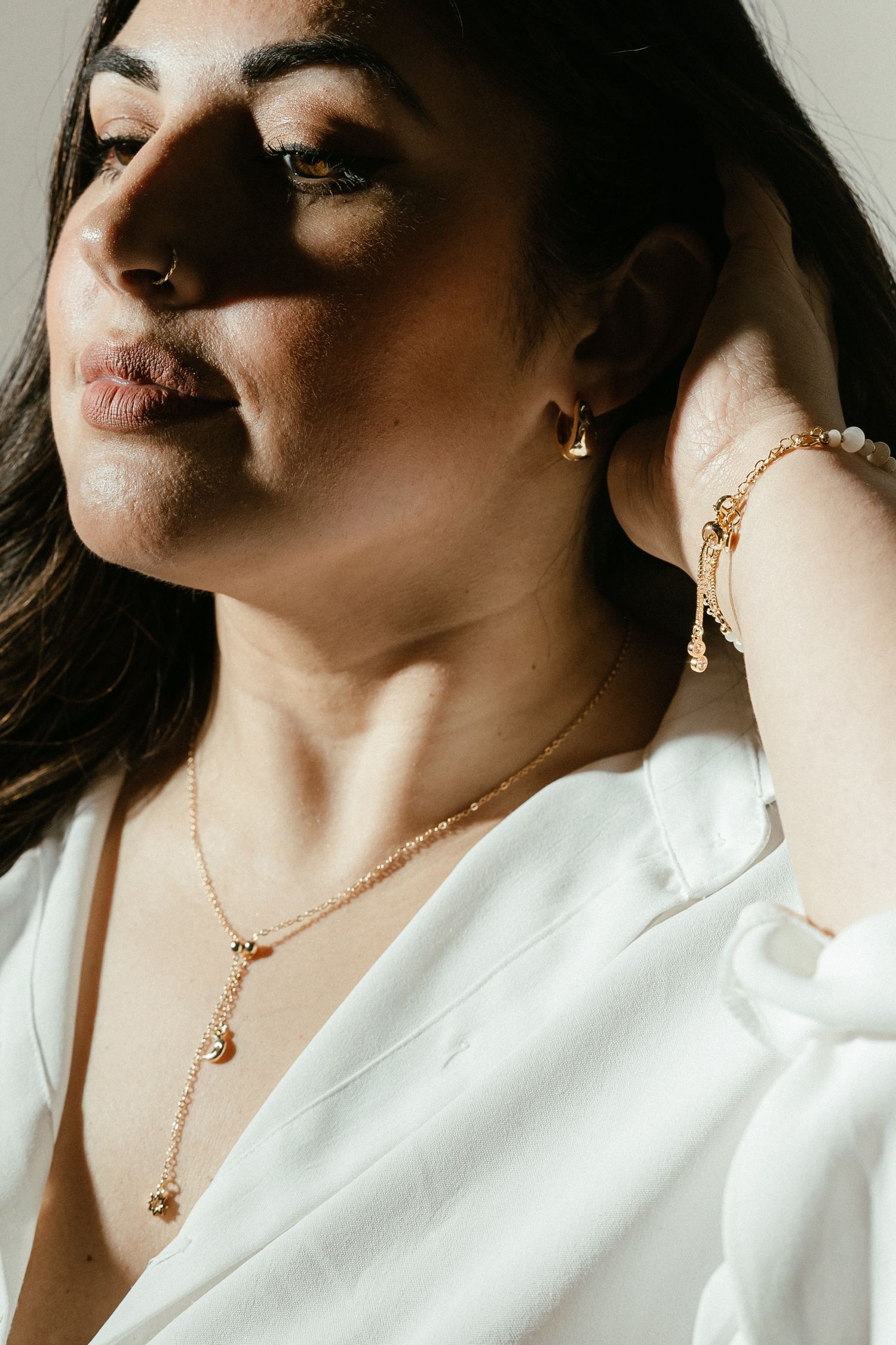 Delicate gold necklace with pendant shown in close-up detail against a white blouse.