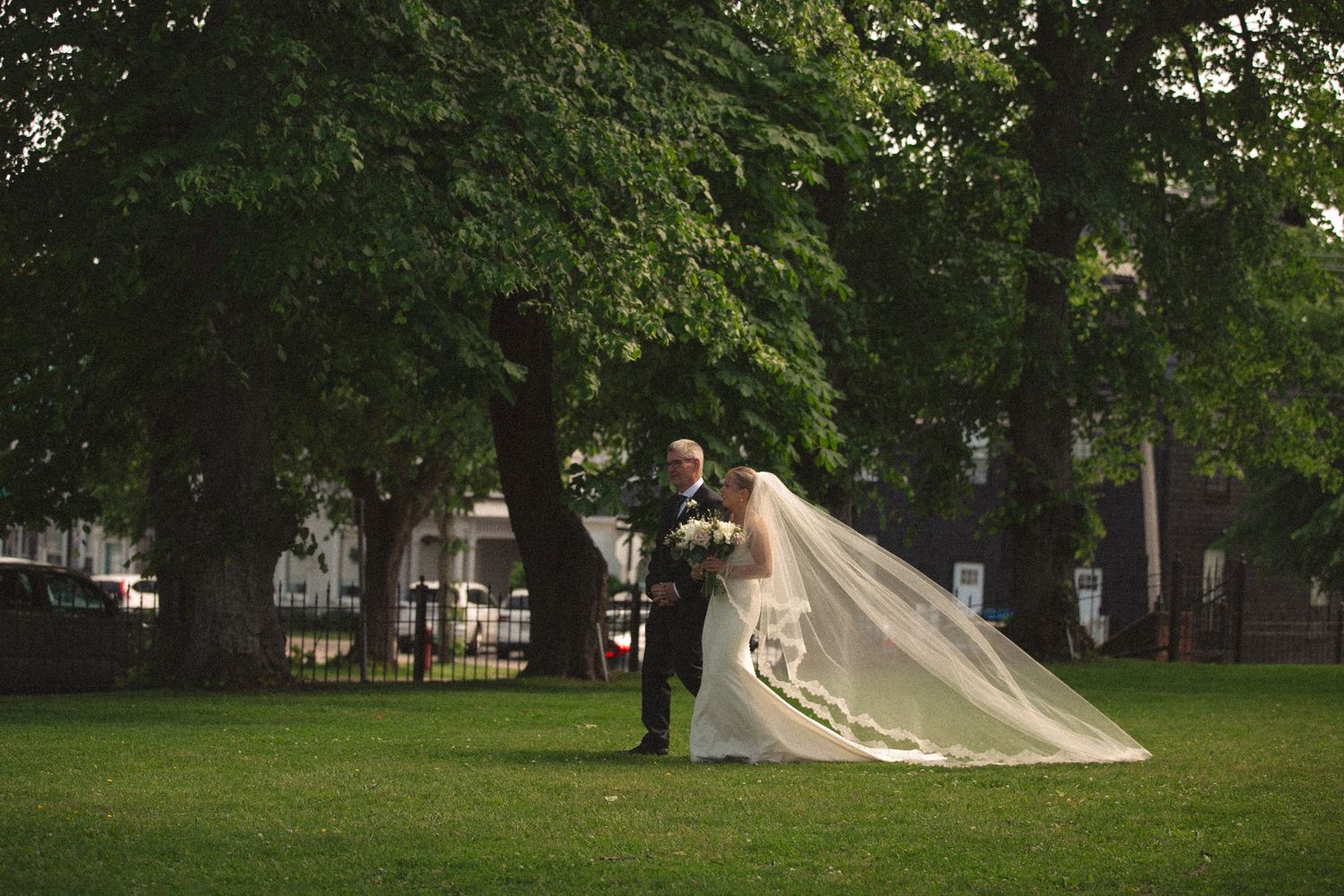 Panoramic view of wedding celebration on sprawling lawn with trees.