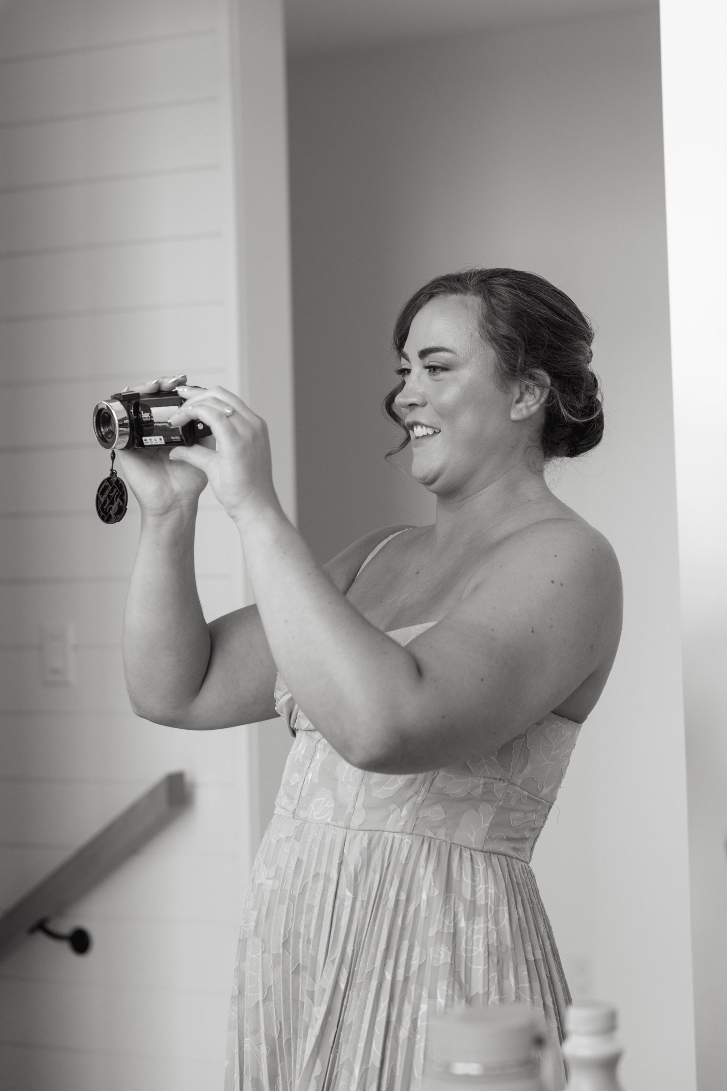 Person in a light colored dress smiles while holding binoculars during wedding preparations.