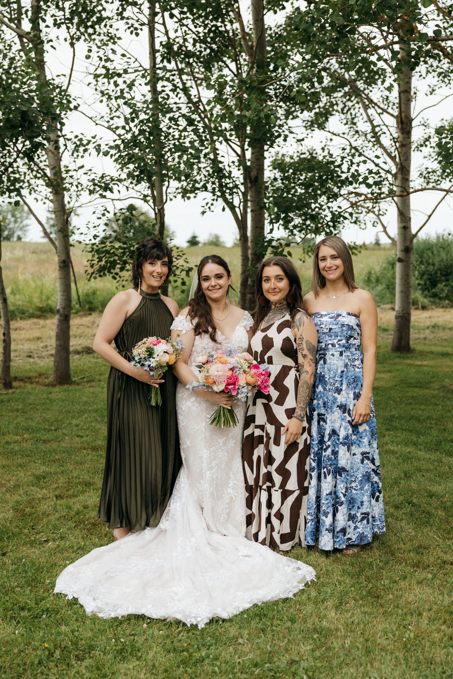 Wedding party members in mix of dark and floral dresses posing with bouquets outdoors.