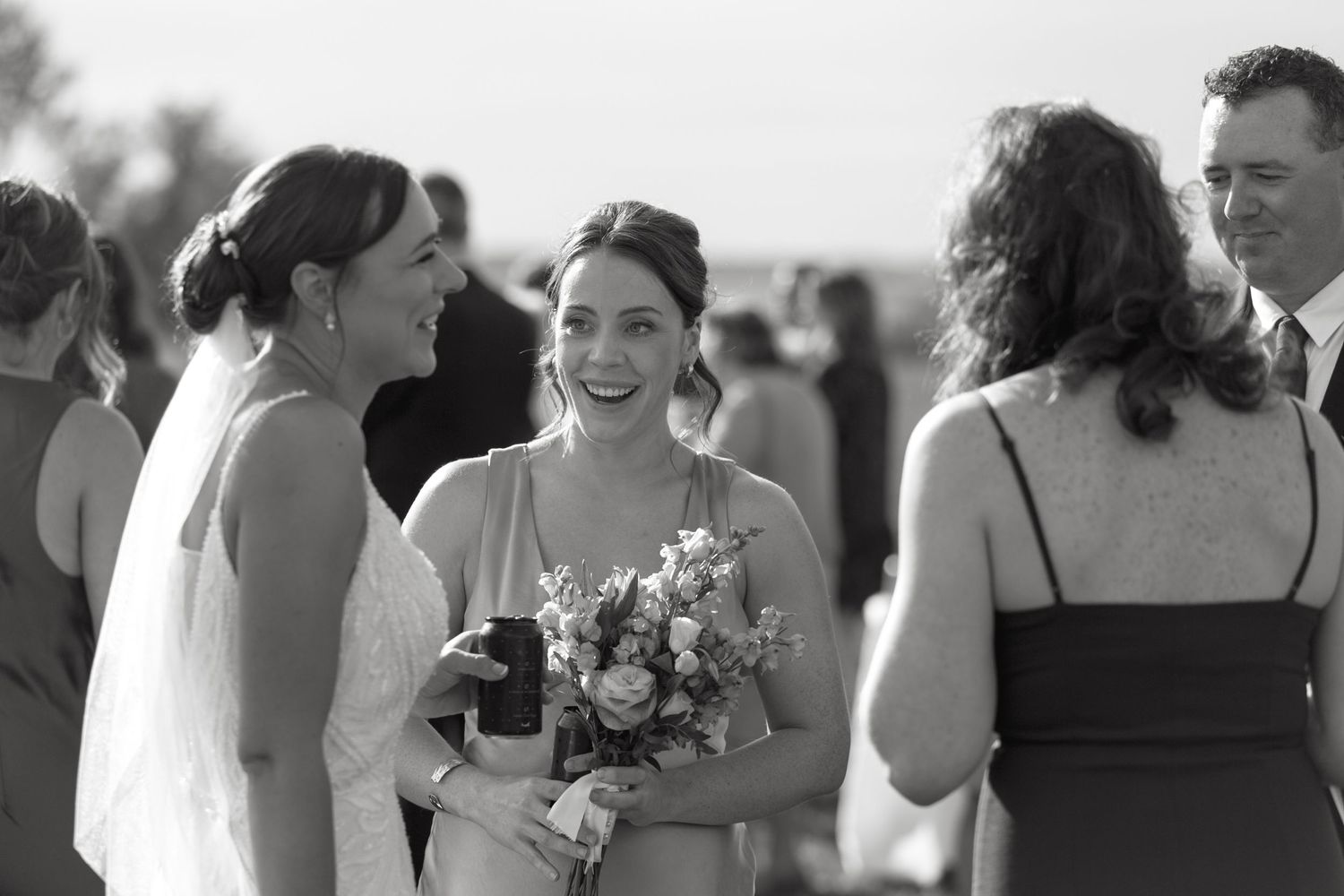 Wedding party members share joyful moments and laughter during outdoor celebration.