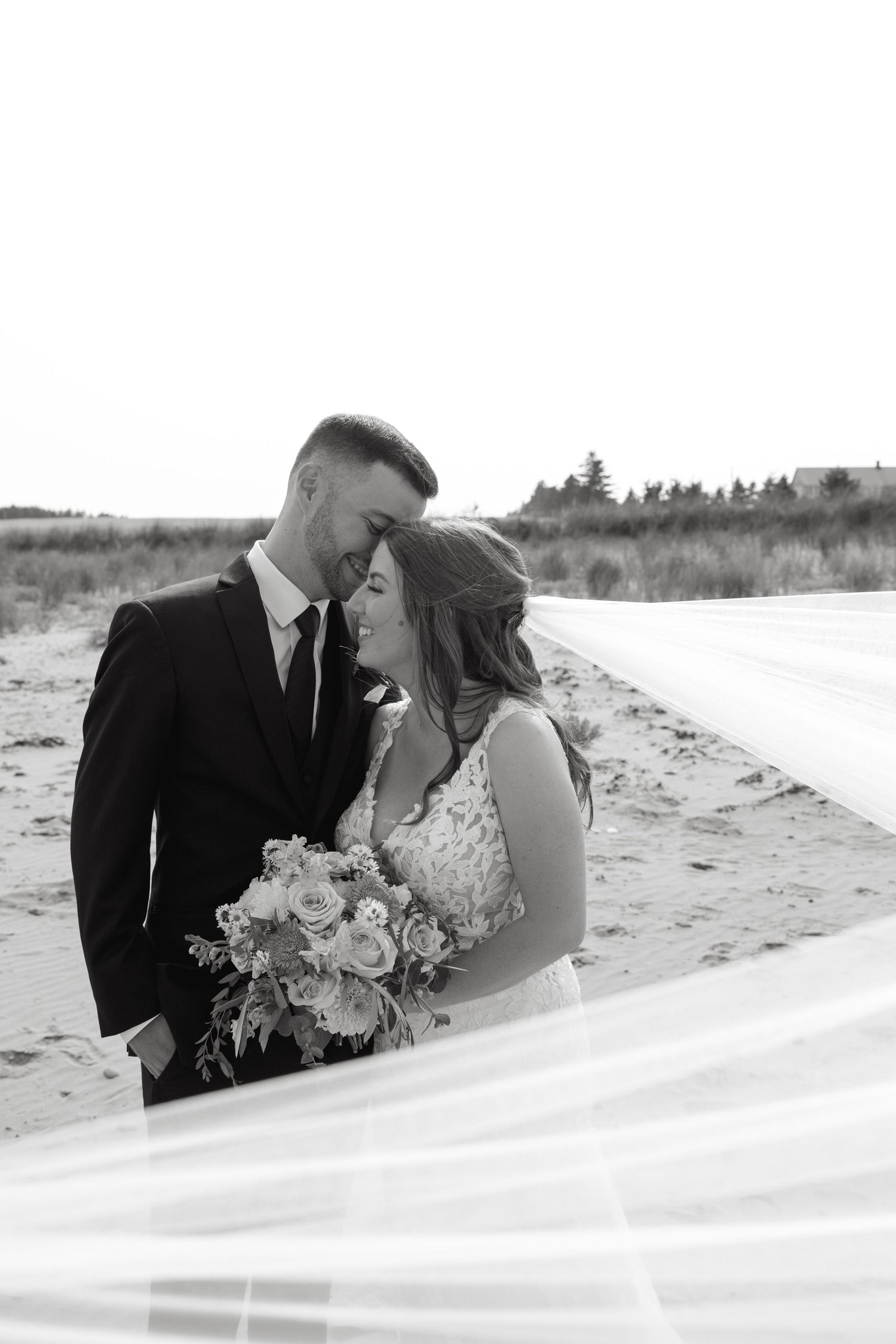 Romantic black and white beach portraits of newlyweds with flowing veil in the sand.