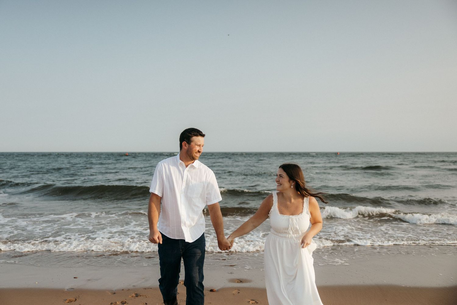 Two people hold hands while walking along a scenic beach at sunset.