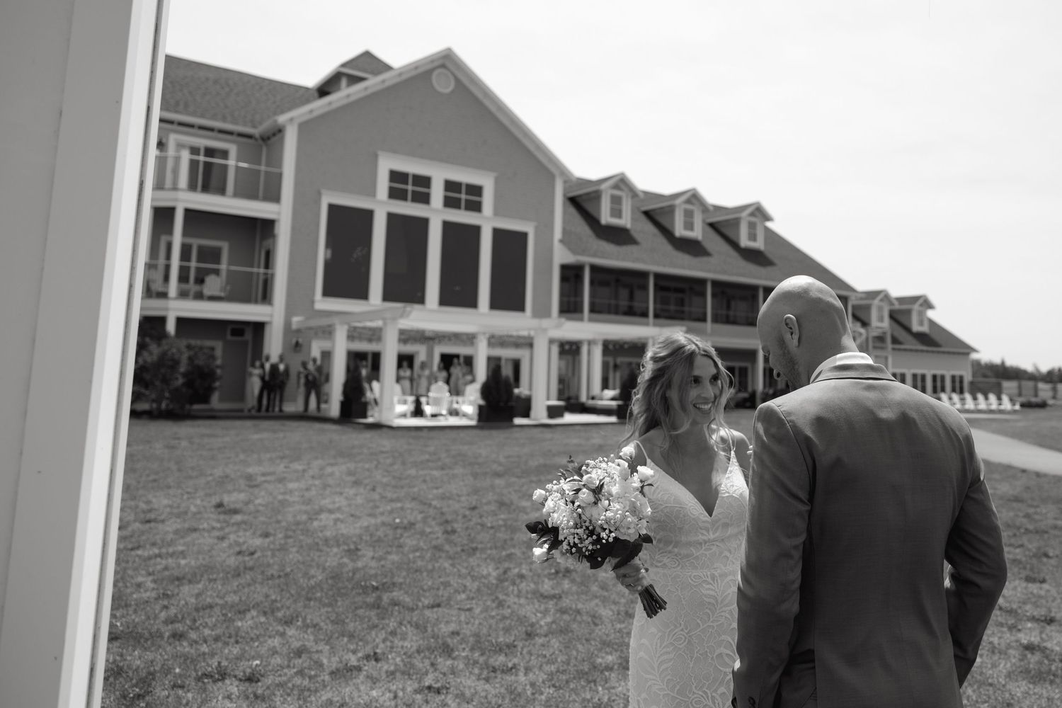 Wedding couple walking towards large house on grassy lawn.
