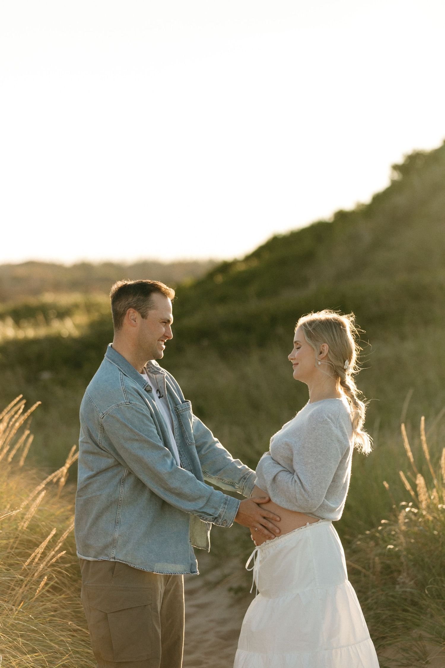 A sunset maternity photo showing a couple embracing among golden grasses.