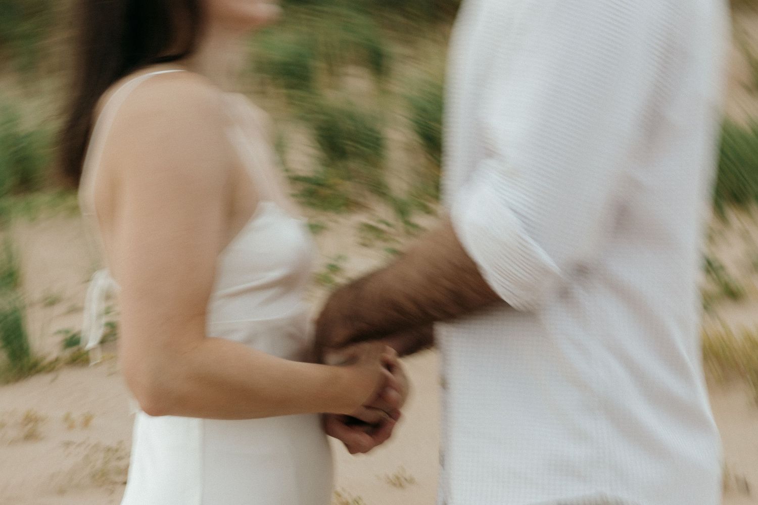 An intimate moment captured between two people in white clothing on sandy dunes.