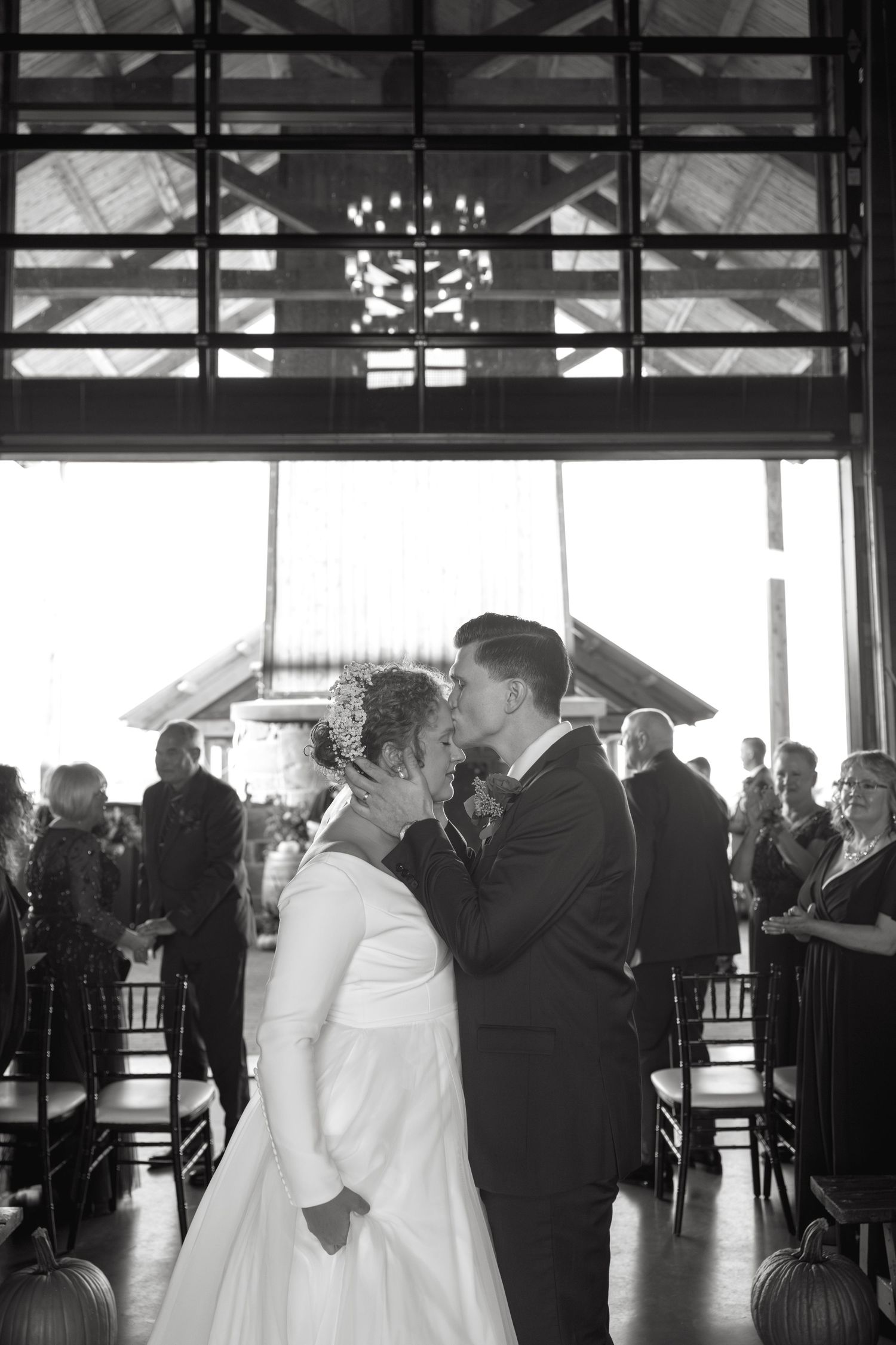 Wedding guests dance and celebrate in a spacious venue with large windows and chandeliers.