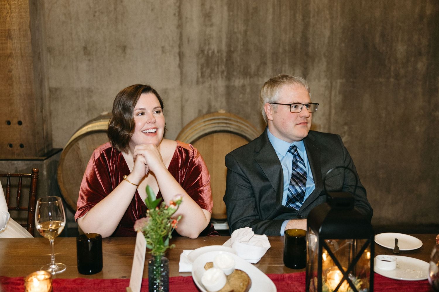 Elegant dinner gathering in wine cellar with guests seated at long table with red linens.