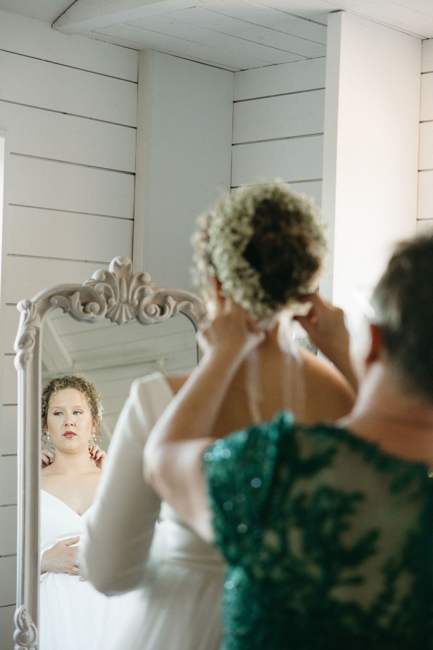 A bride looks at her reflection in an ornate white mirror while getting ready.