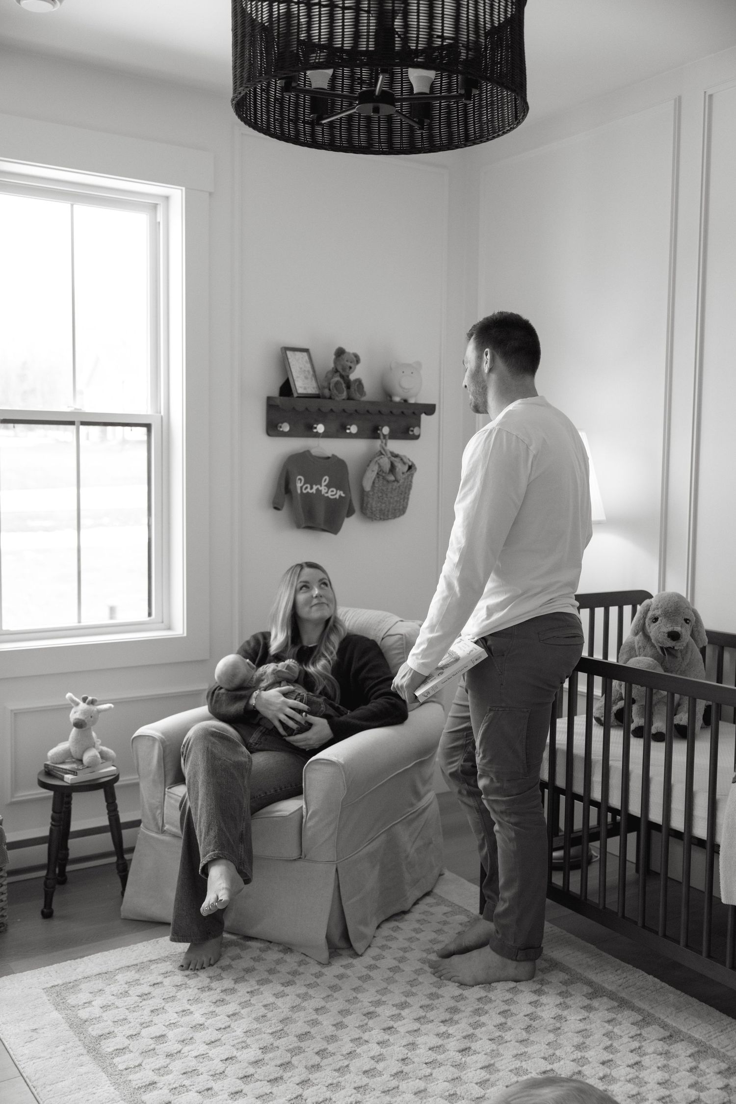 A black and white nursery scene with a dramatic black pendant light and wooden baby crib.