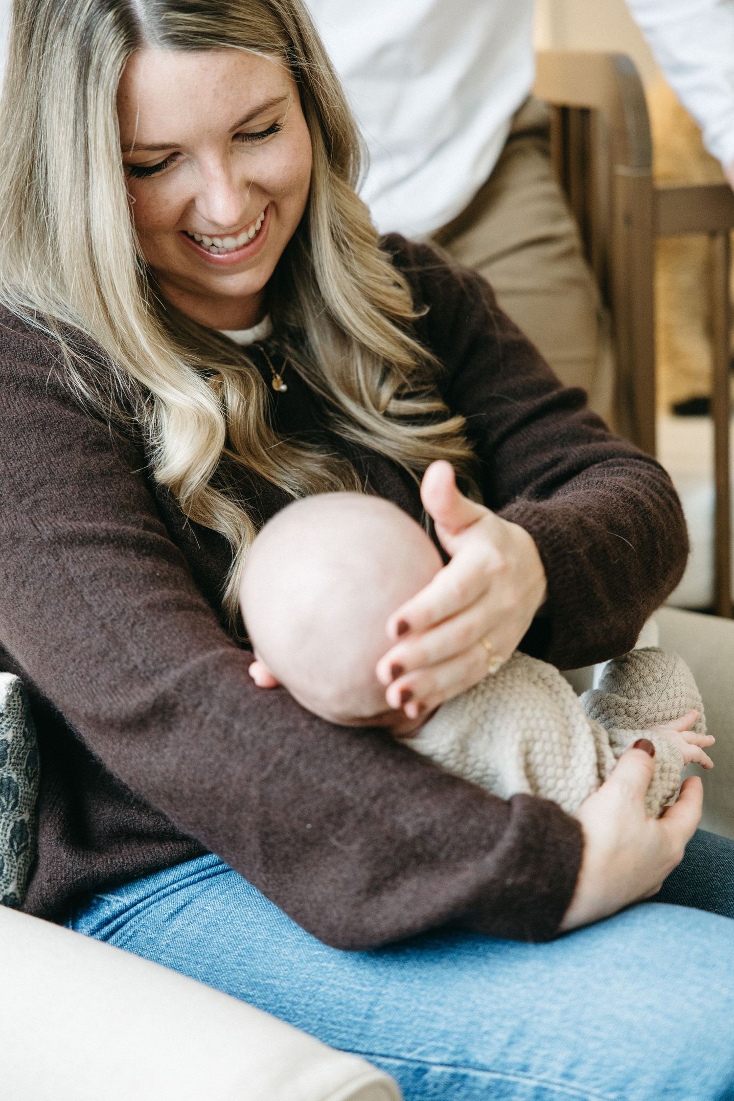Woman in brown sweater tenderly holding infant while sitting in casual attire.
