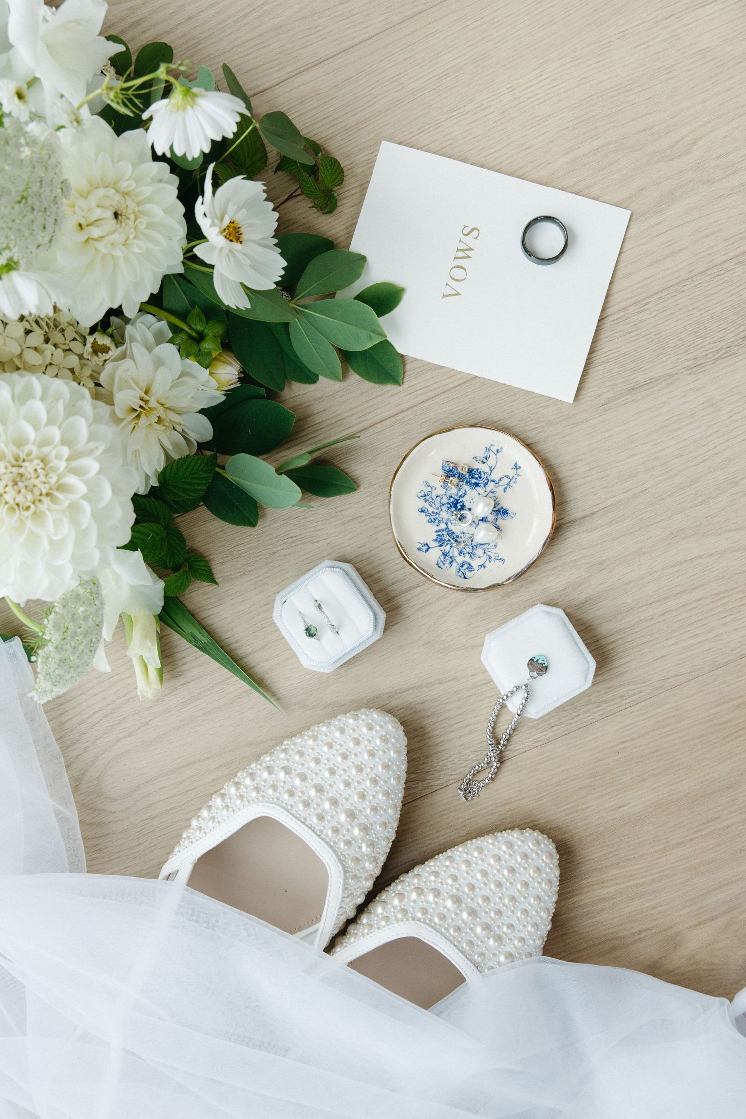 Wedding accessories including white shoes, rings, and delicate floral arrangements on a light wooden surface.