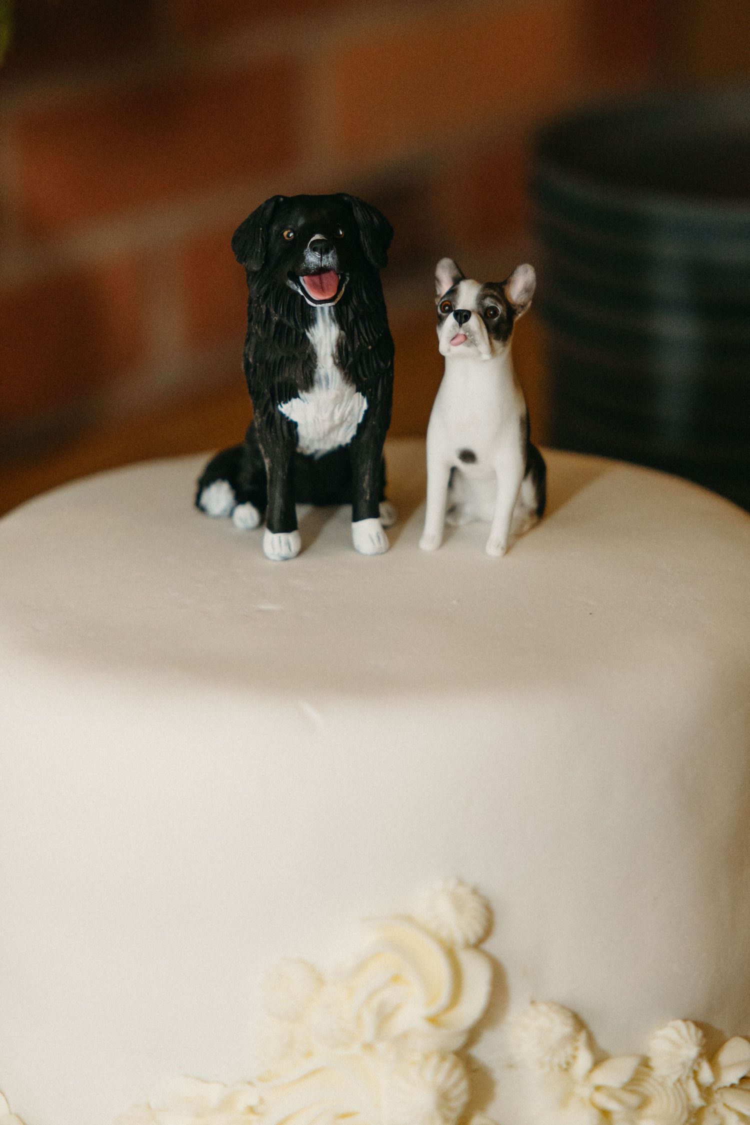 Two dog figurine cake toppers, a black and white fluffy dog and a Boston terrier, sit on a white fondant wedding cake.