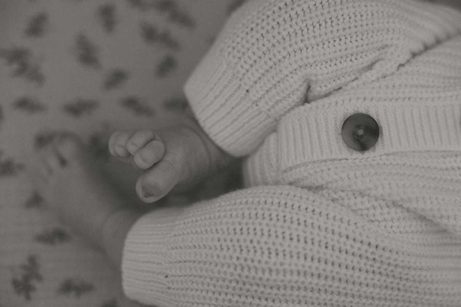 Close-up black and white photo of a tiny hand against a knit white sweater.