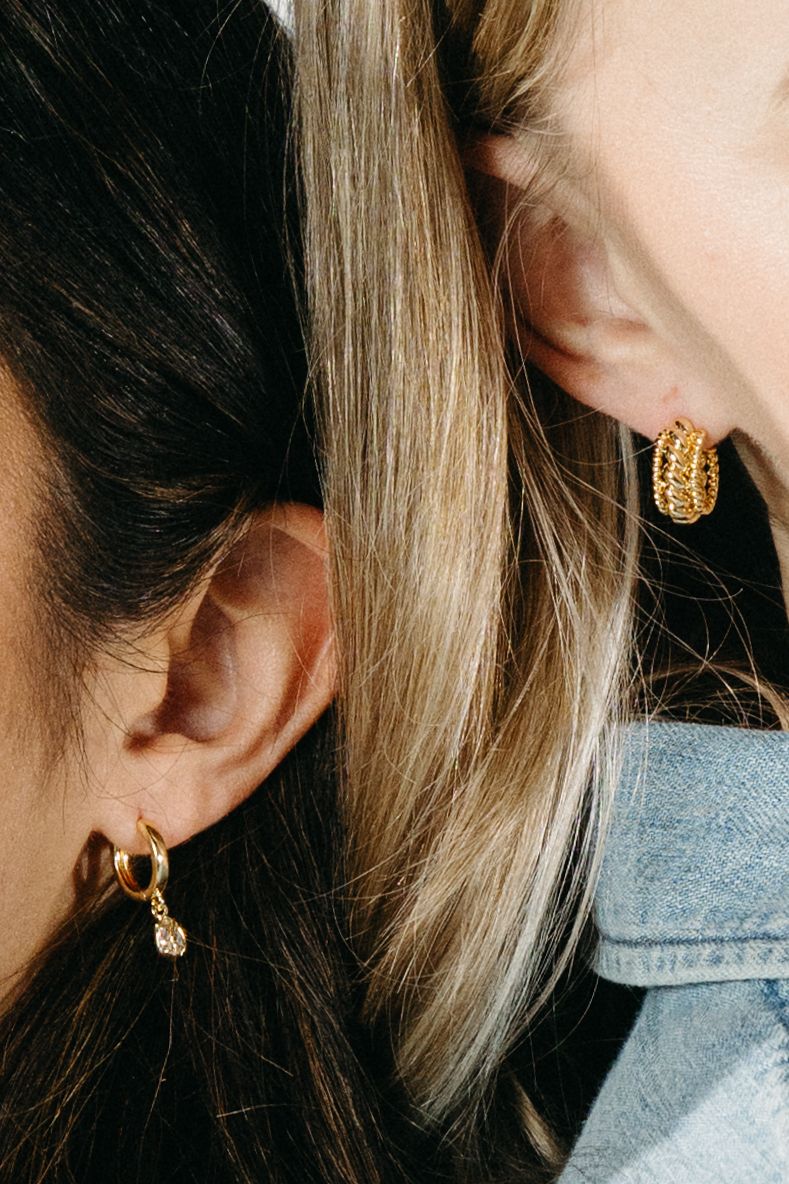 Close-up view of various gold hoop earrings displayed on ears against a light blue background.