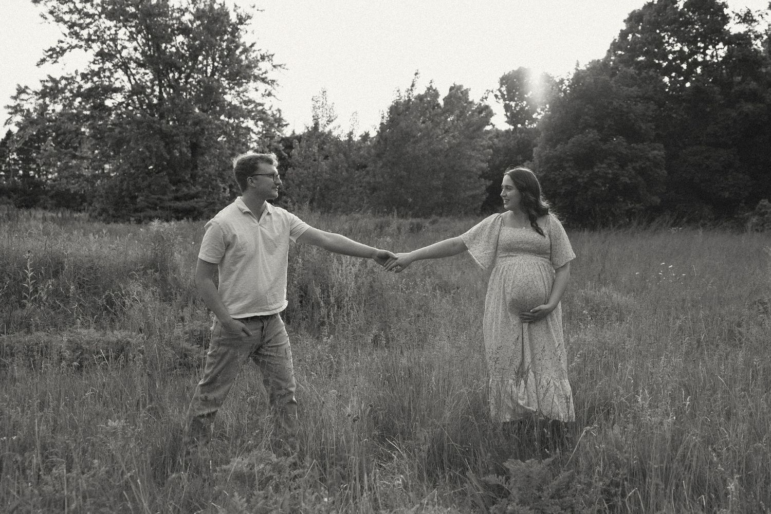 Black and white photo of a couple holding hands in a grassy meadow, with the woman wearing a flowing dress.