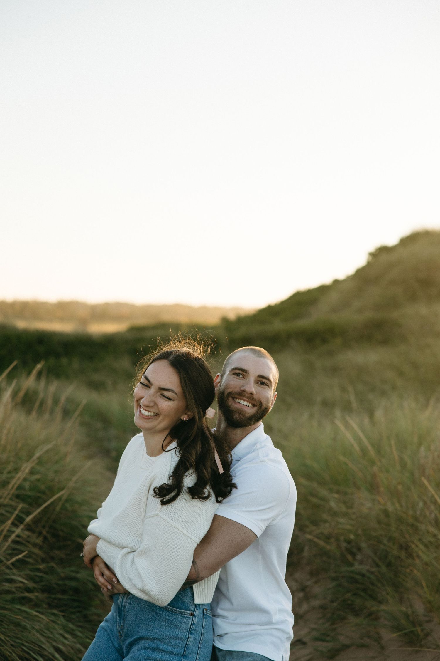 Playful couple sharing laughter among coastal dunes at sunset.
