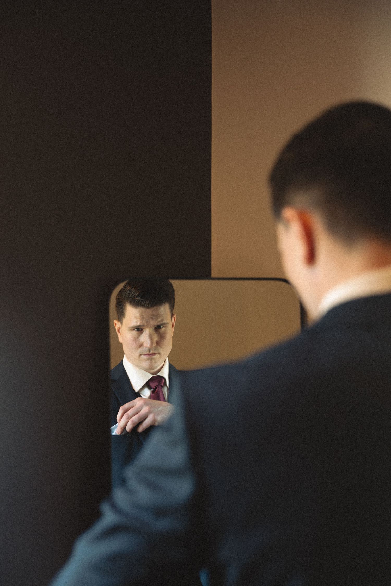 A groom adjusts his tie while getting ready in a dimly lit room.