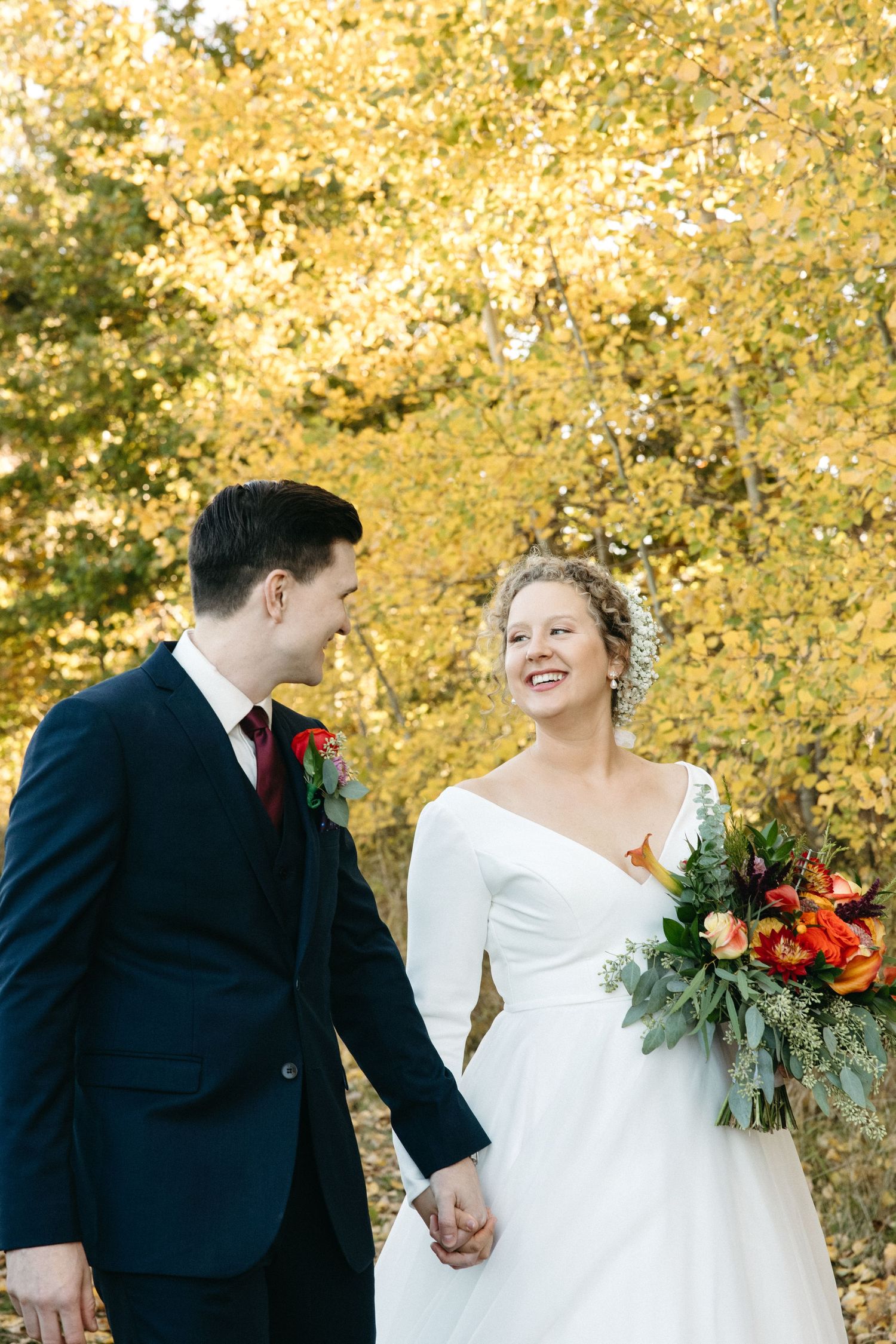 Joyful wedding couple laughing together against backdrop of golden autumn leaves.