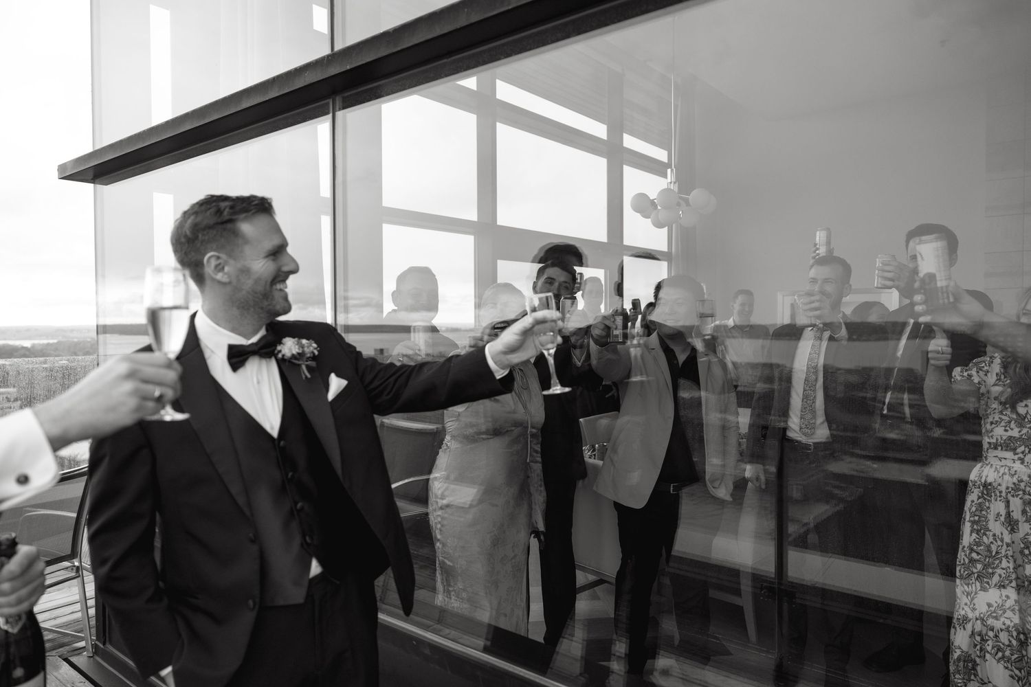 Group of people socializing in a bright room with floor-to-ceiling windows.