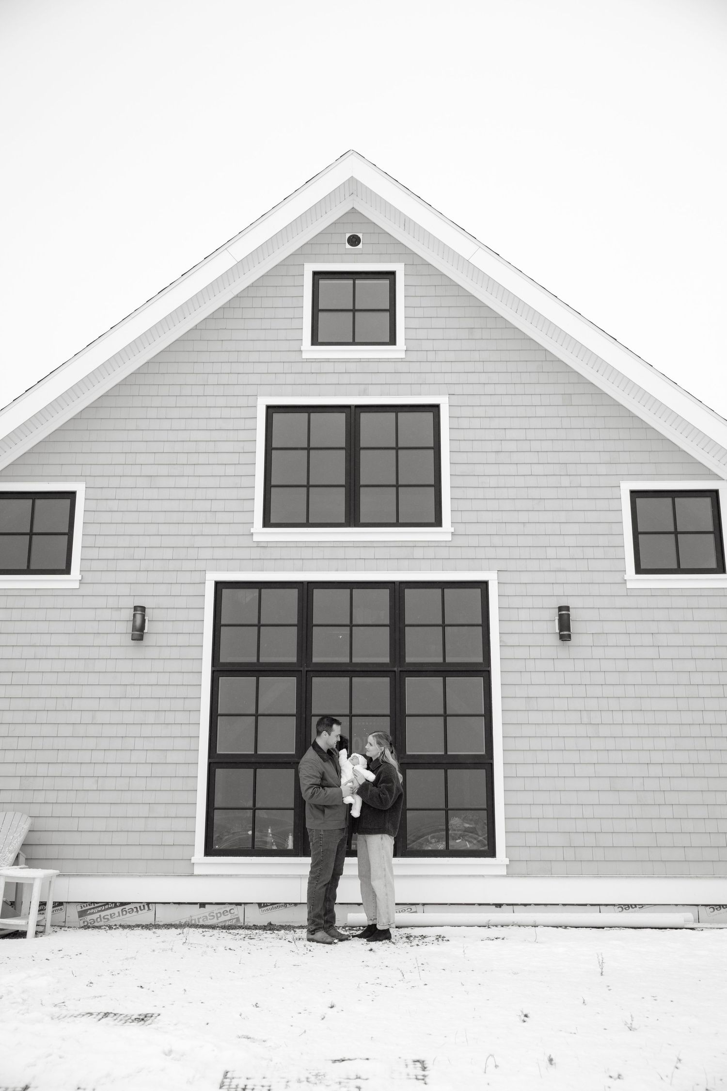 A modern white barn-style house with large black-framed windows and two people standing outside.