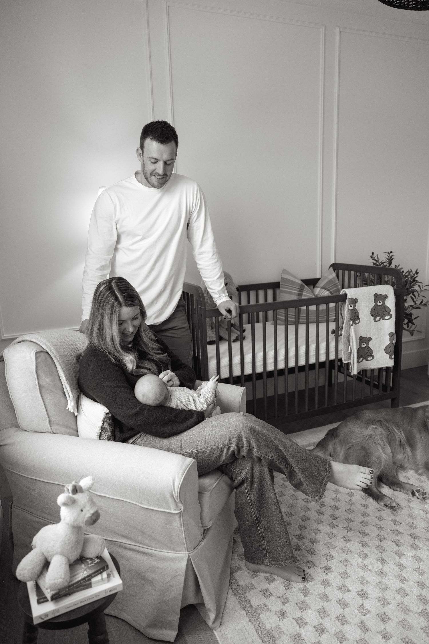 Black and white nursery scene with parents and baby relaxing on white furniture.