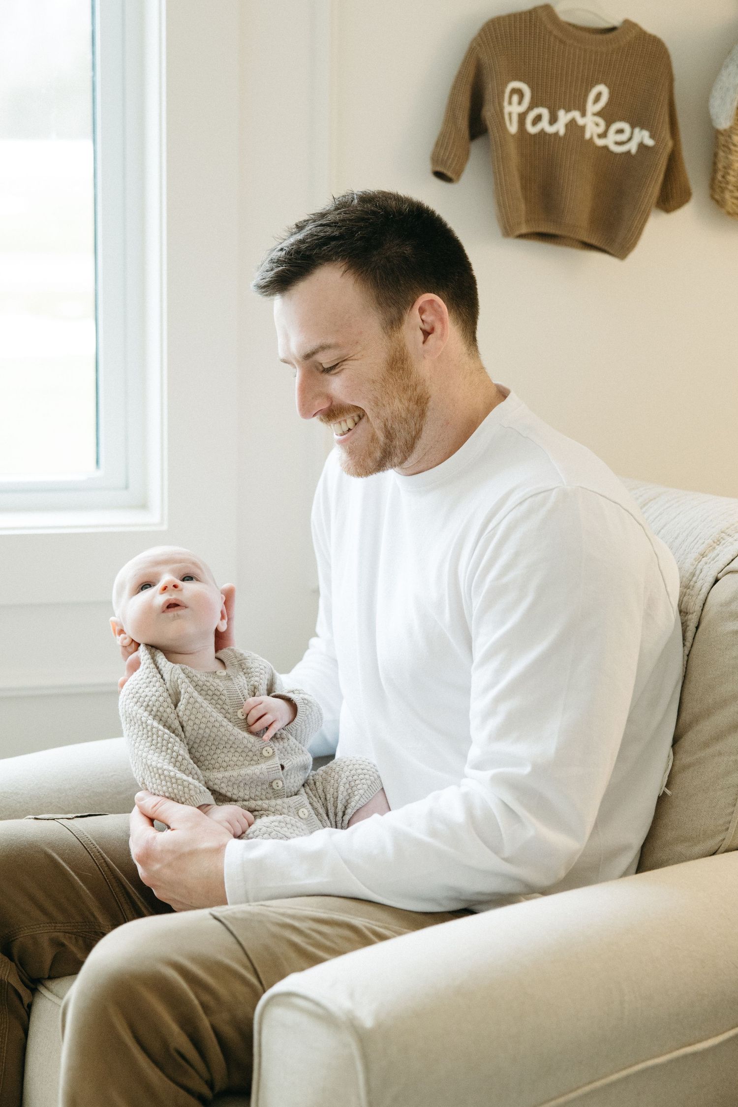 Heartwarming moments shared on beige couch with baby in knit sweater.