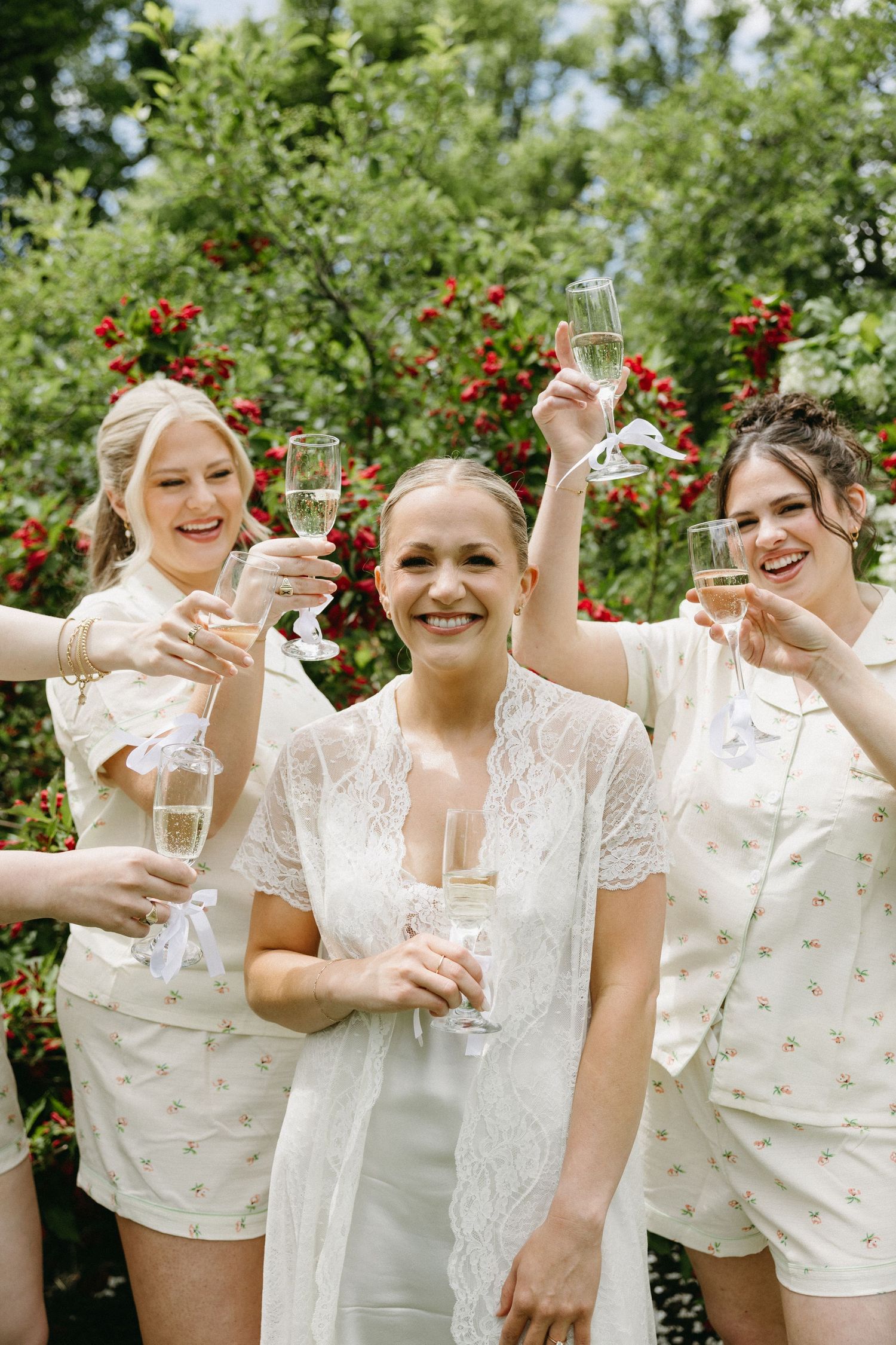 Wedding party in cream-colored outfits toasting with champagne glasses in a garden.