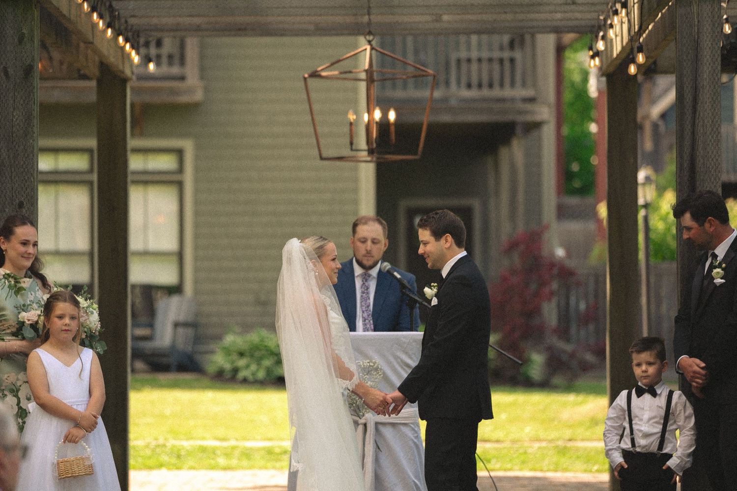 Wedding ceremony guests seated outdoors in white chairs on a sunny day.