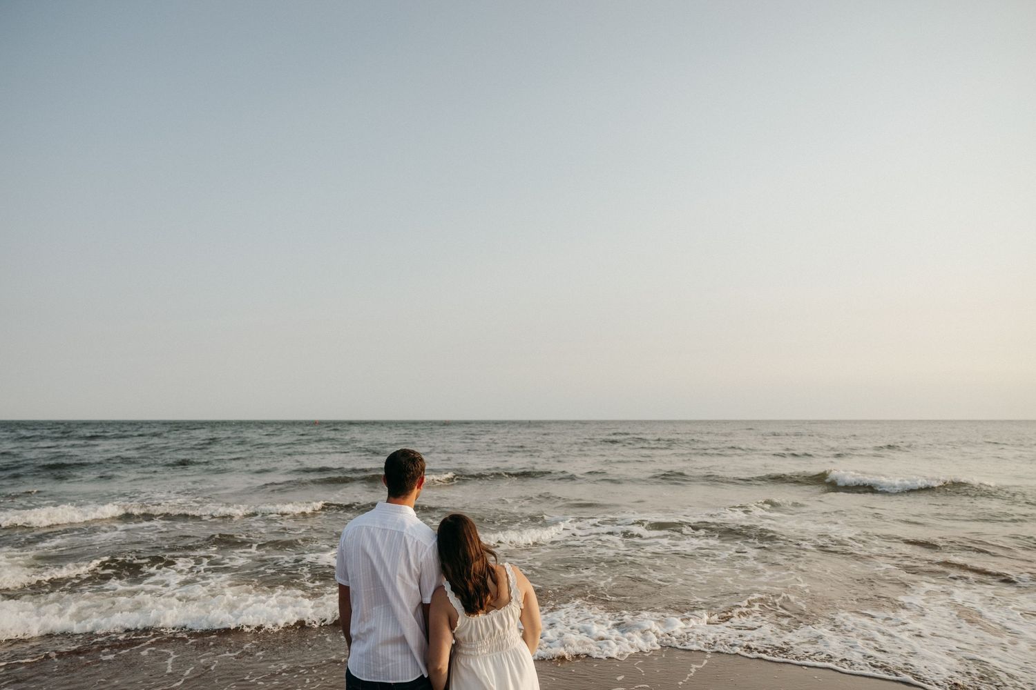 Two people gaze at the ocean horizon while standing on a beach.