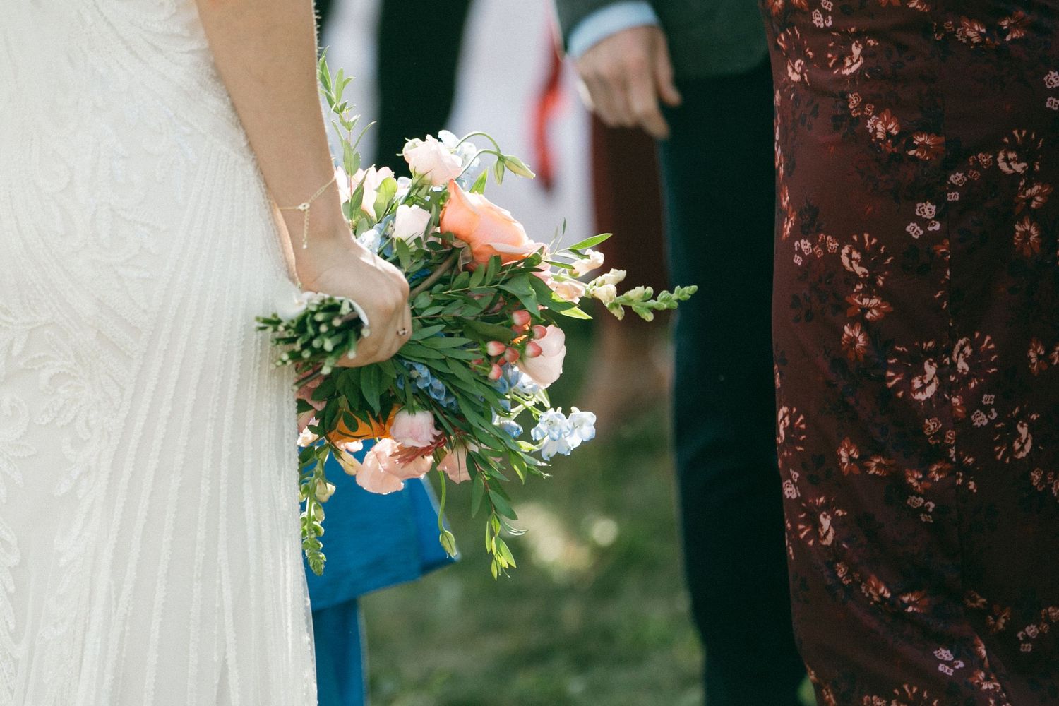 Wedding party members hold colorful floral bouquets against natural backdrop.