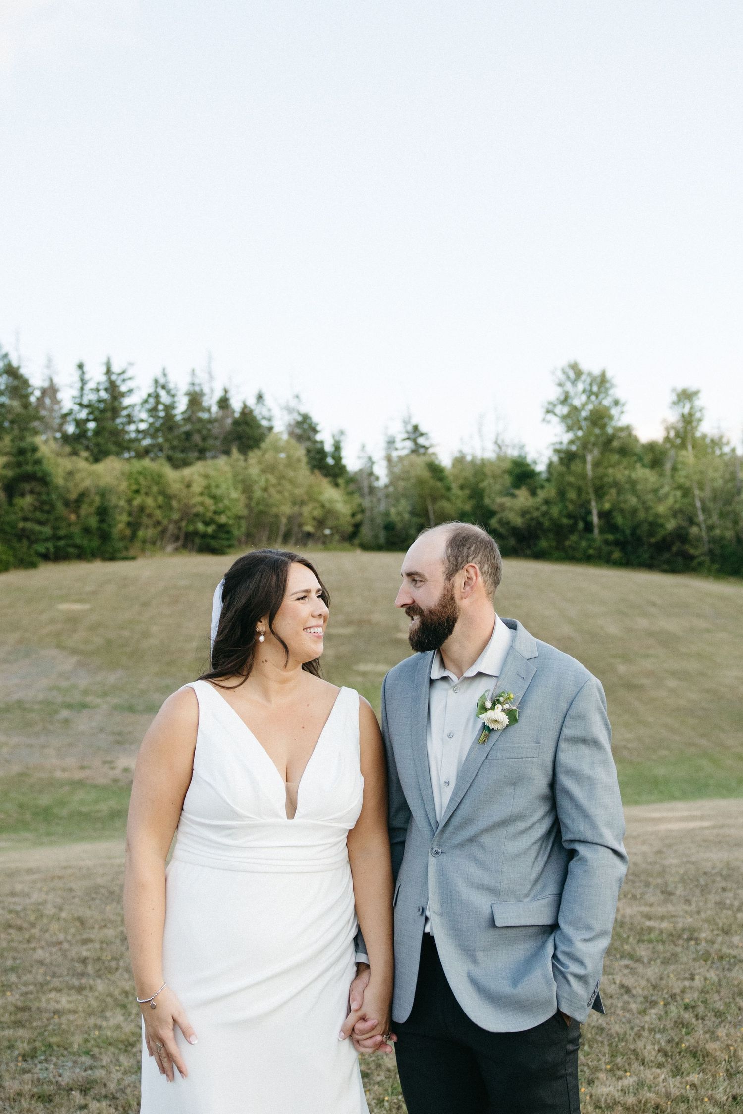A couple shares a joyful moment together on a grassy hillside during their wedding photoshoot.
