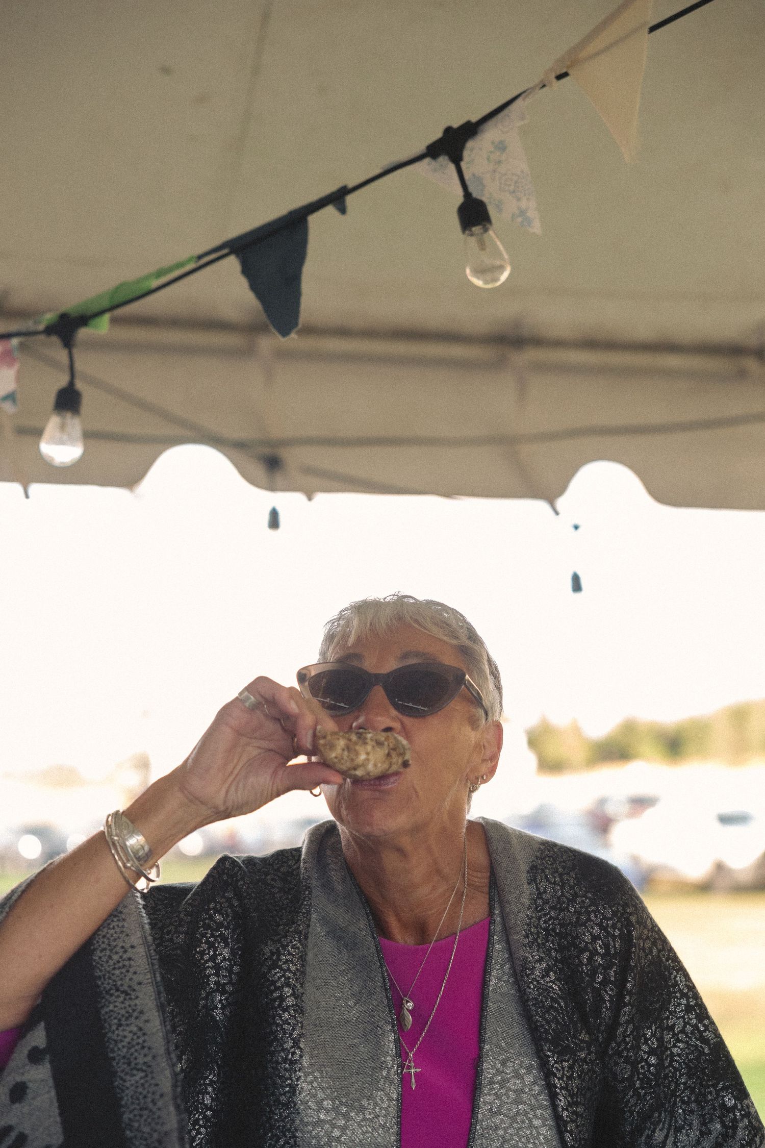 Person in sunglasses and sparkly jacket enjoying a drink at an outdoor event.