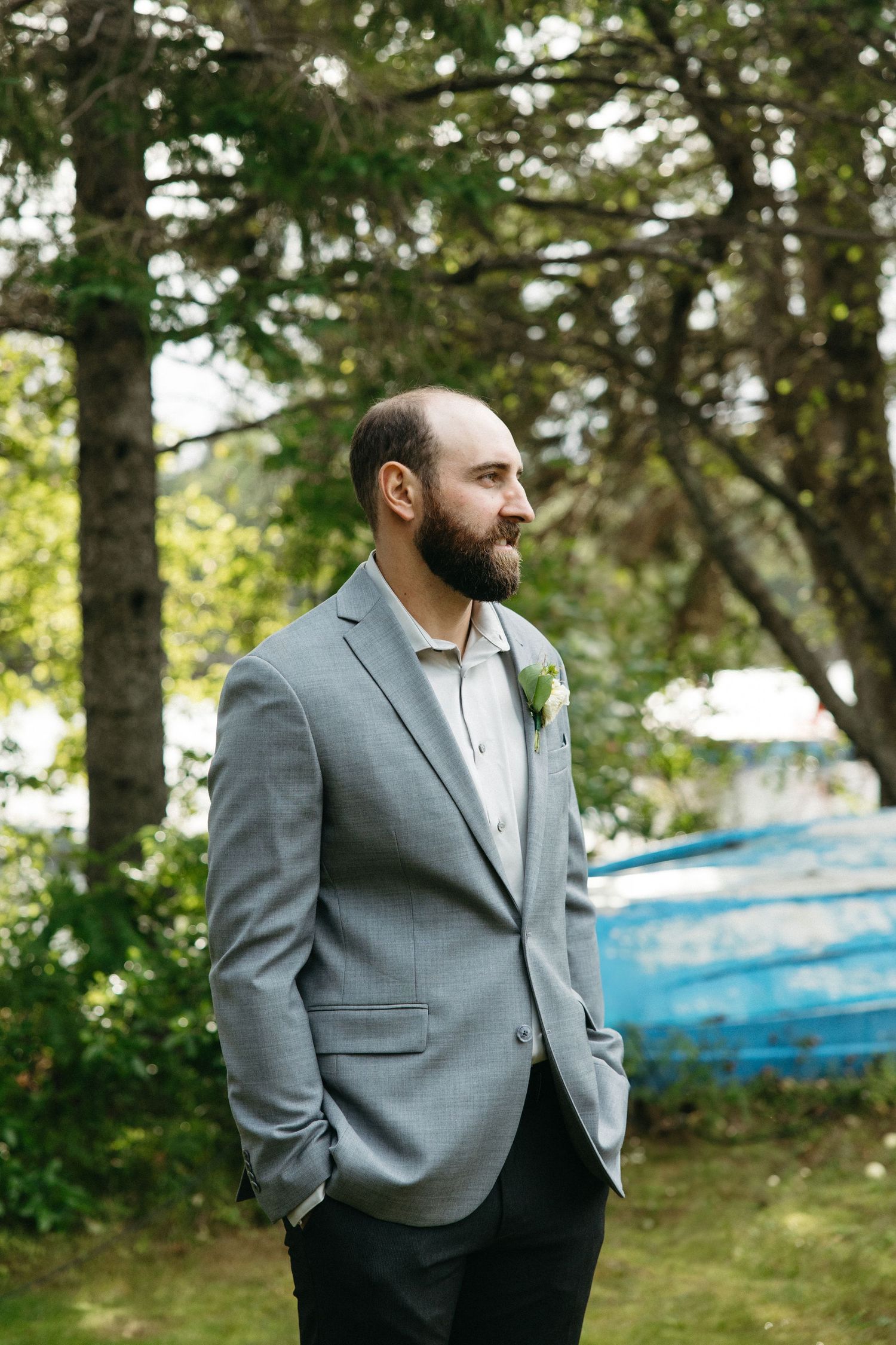 A person in a gray suit jacket stands in an outdoor setting with trees in the background.